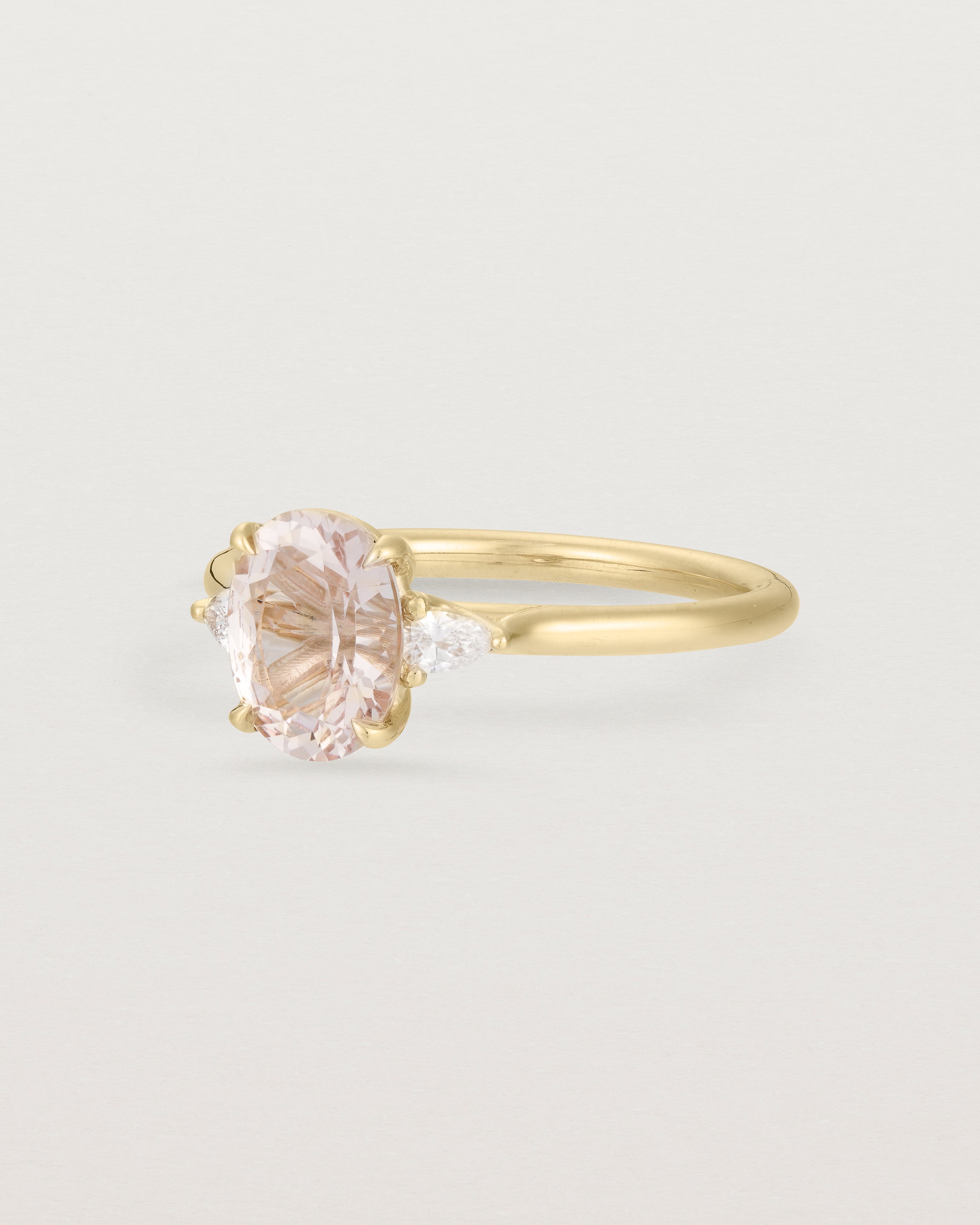 The side view of An oval morganite adorned with white diamonds either side, featuring a sweeping setting and crafted in yellow gold