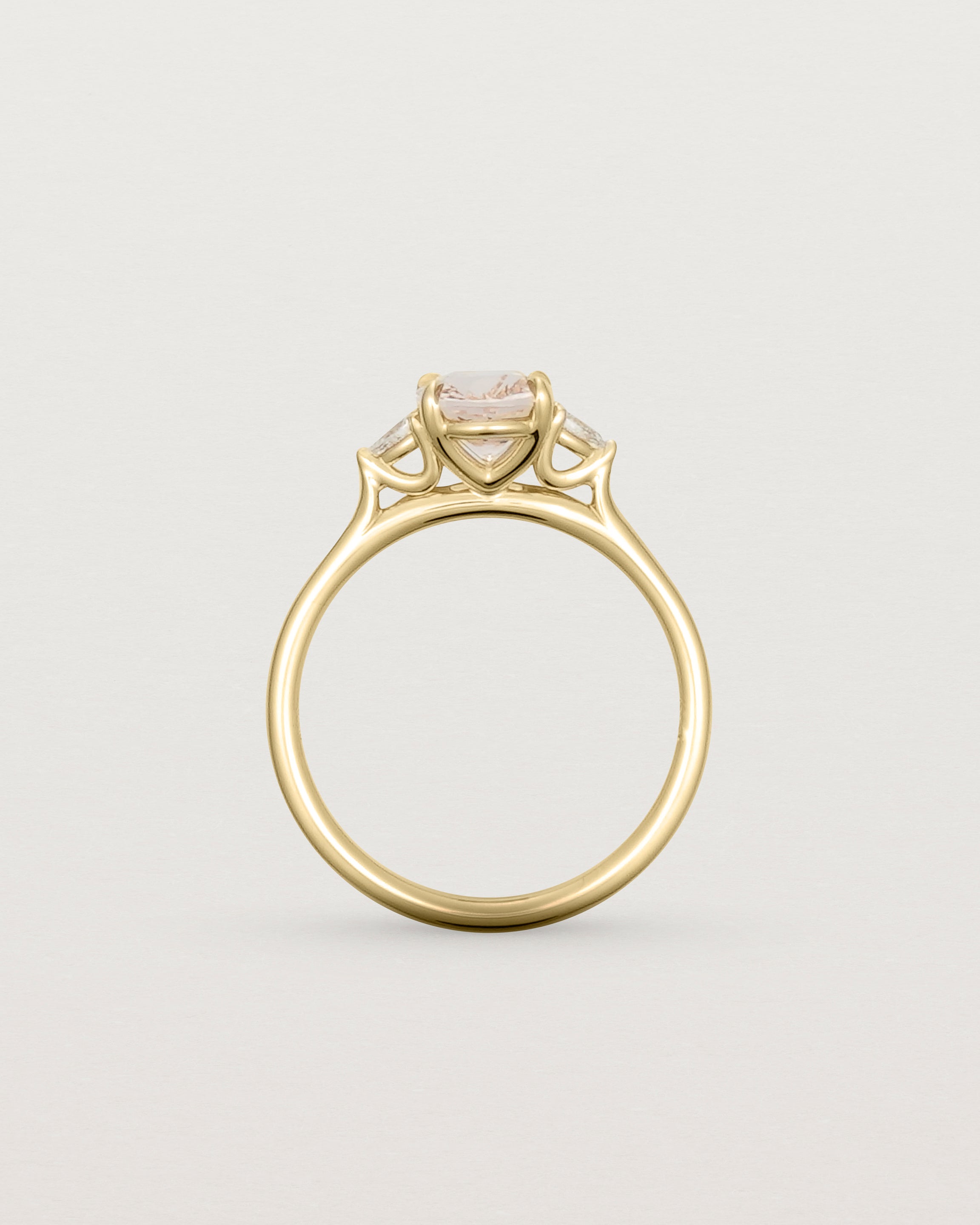 The side profile of an oval morganite adorned with white diamonds either side, featuring a sweeping setting and crafted in yellow gold