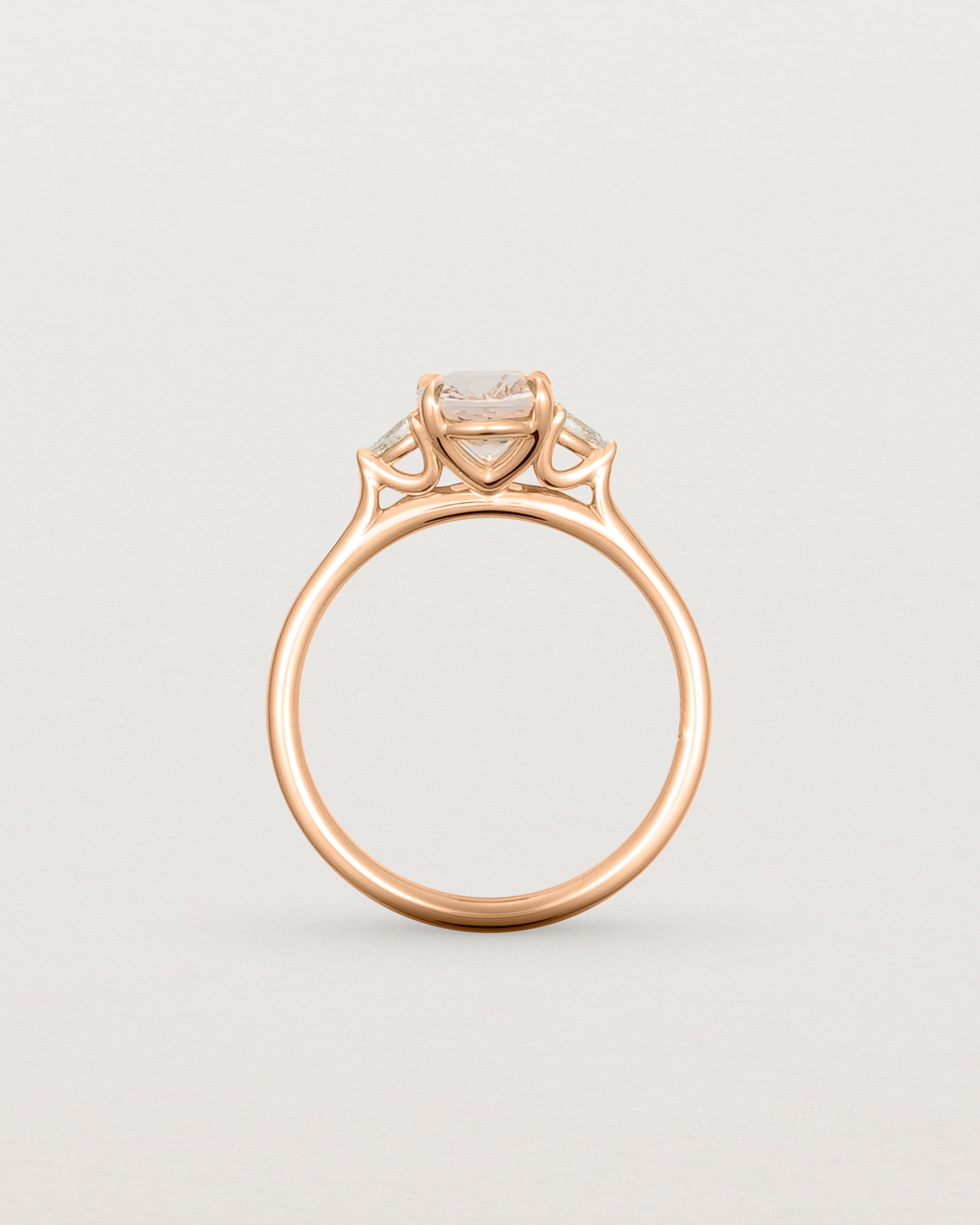 Side profile of an oval morganite adorned with white diamonds on either side, featuring a sweeping setting and crafted in rose gold