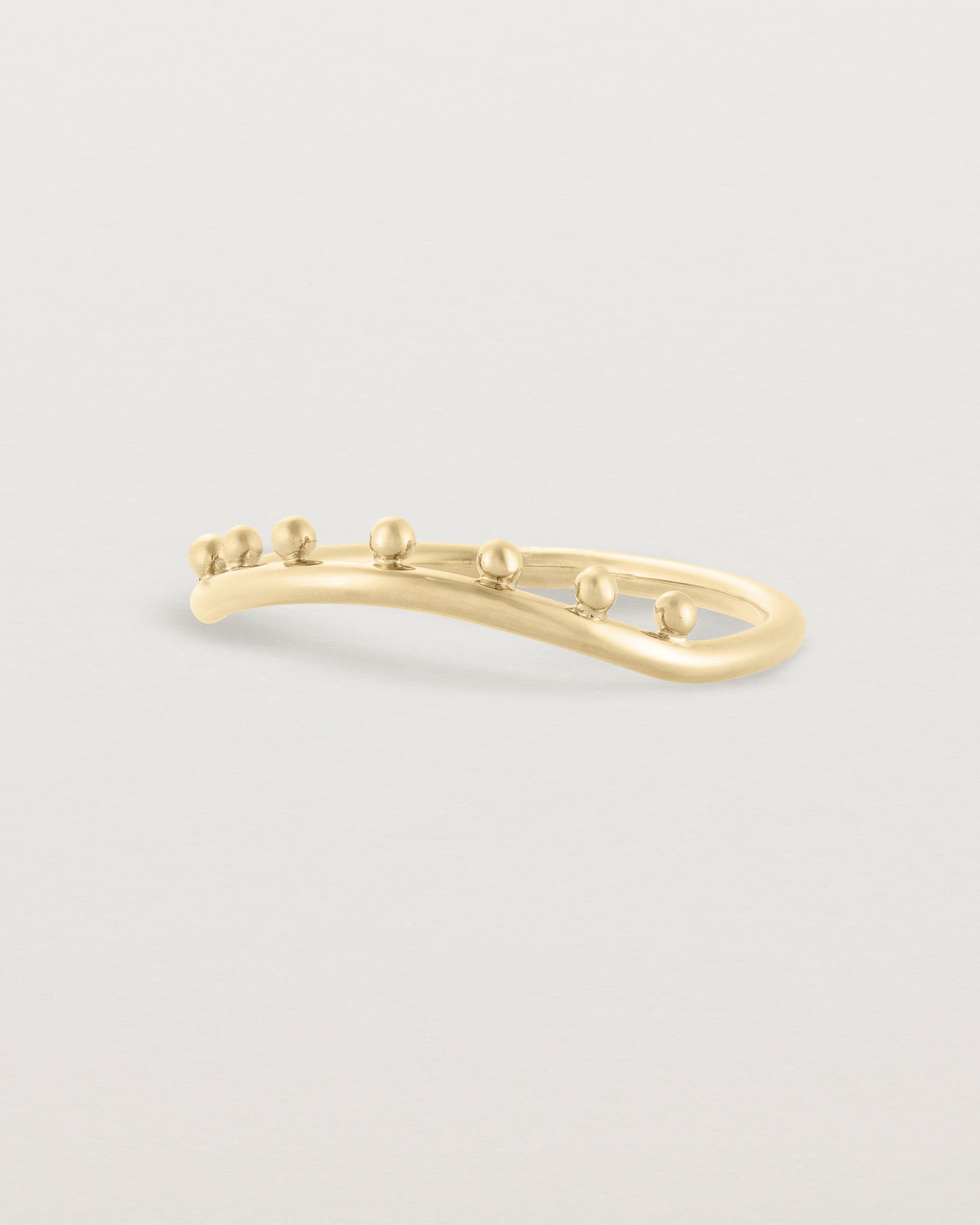 The side view of a gentle arc ring with dot detailing along the top of the arc, crafted in yellow gold