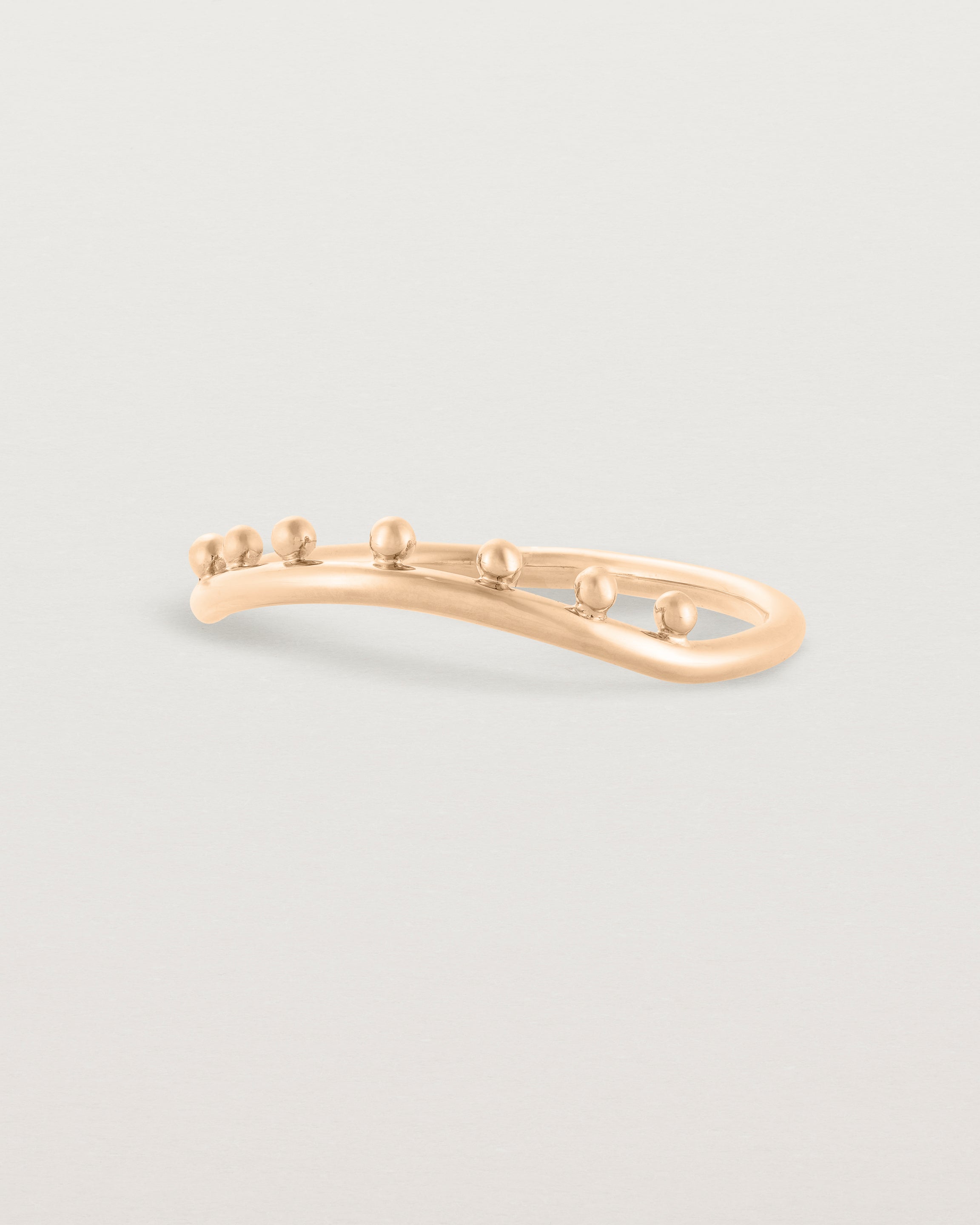 Side view of a gentle arc ring featuring dot detailing along the top of the arc, crafted in rose gold.