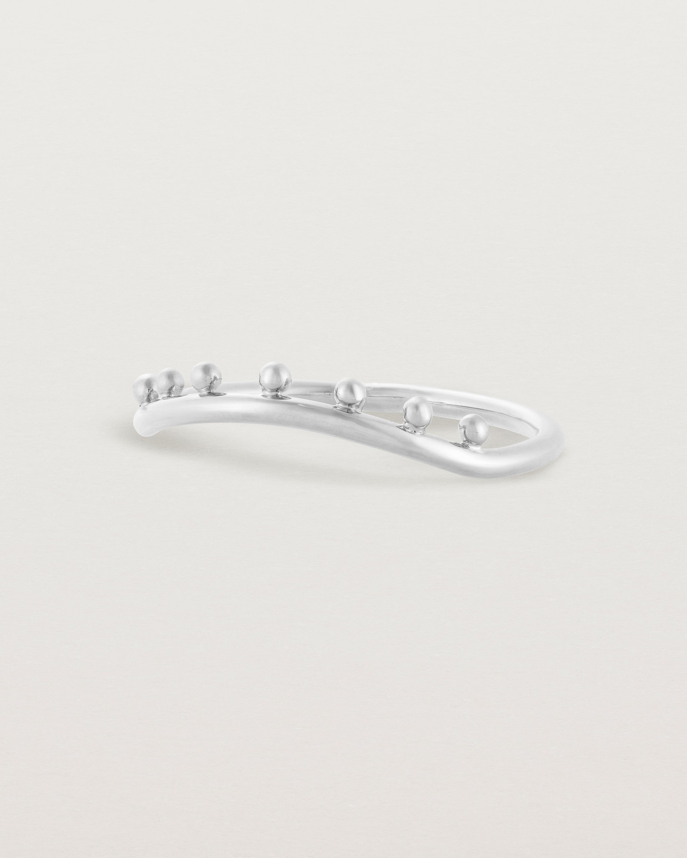 The side view of a gentle arc ring featuring dot detailing along the top of the arc, crafted in white gold.