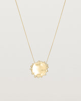 A molten textured yellow gold disc with dots around the circumstance on a yellow gold fine chain necklace