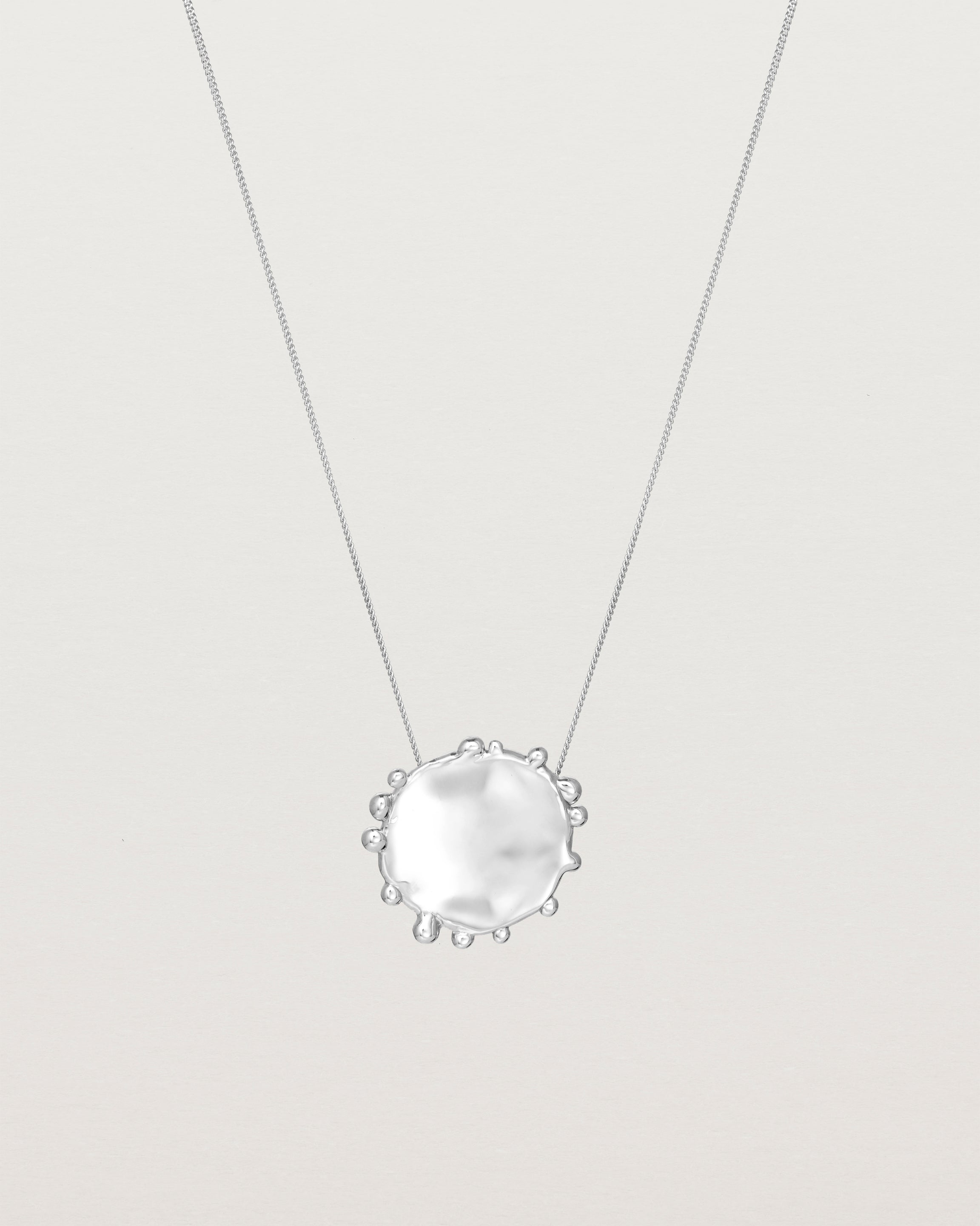 A molten textured silver disc with dots around the circumstance on a silver fine chain necklace