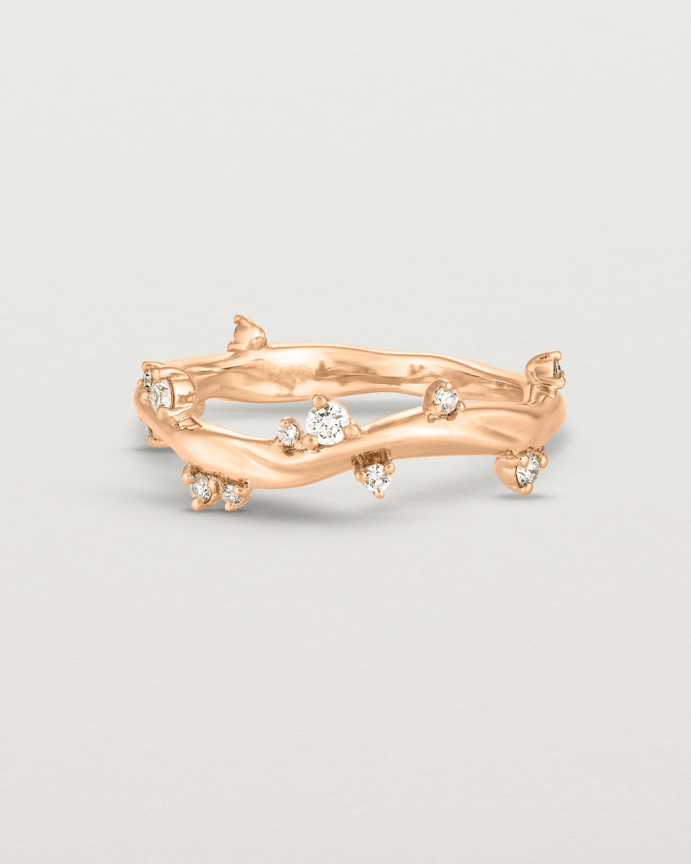 Product photo of the rose gold Ember ring with white diamonds scattered around the band.