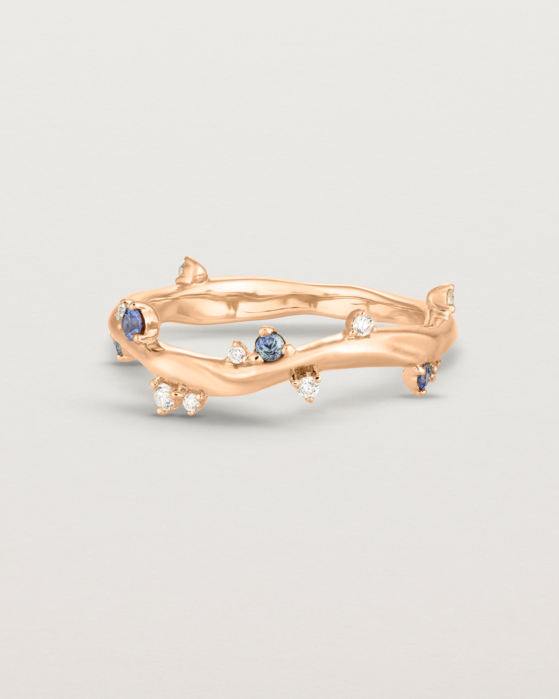 Front image of the Ember ring in rose gold featuring a scattering of white diamonds and blue sapphires.