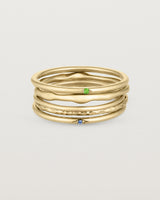 A set of five yellow gold bands, one featuring a blue sapphire, one featuring a green emerald, one textured and two plain