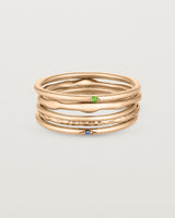 A set of five rose gold bands, one featuring a blue sapphire, one featuring a green emerald, one textured and two plain