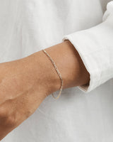 A woman wearing the Figaro Chain Bracelet in yellow gold.