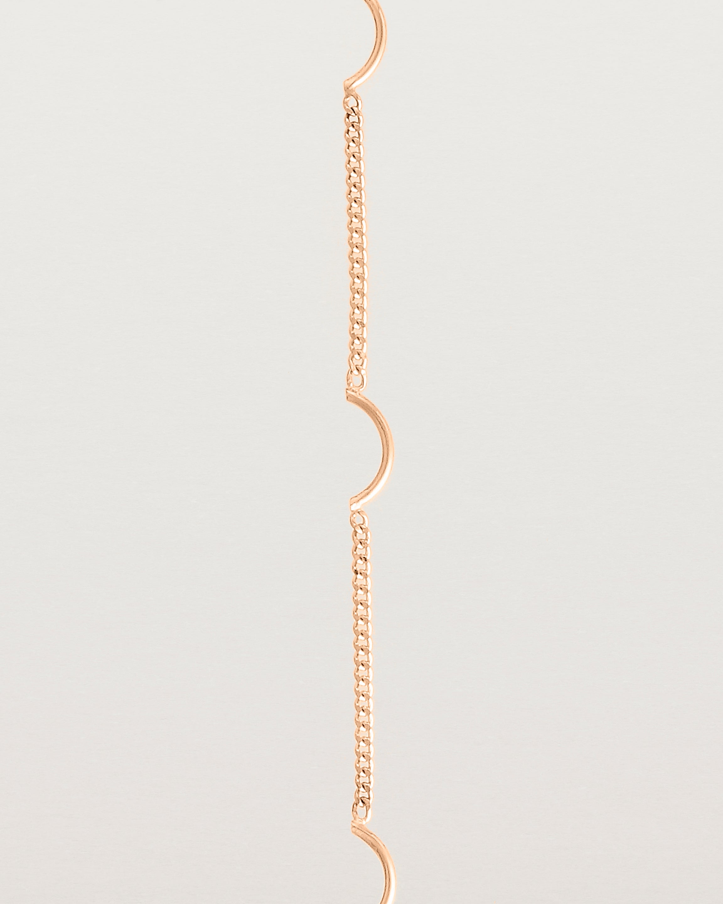 A rose gold chain bracelet with five gold arcs