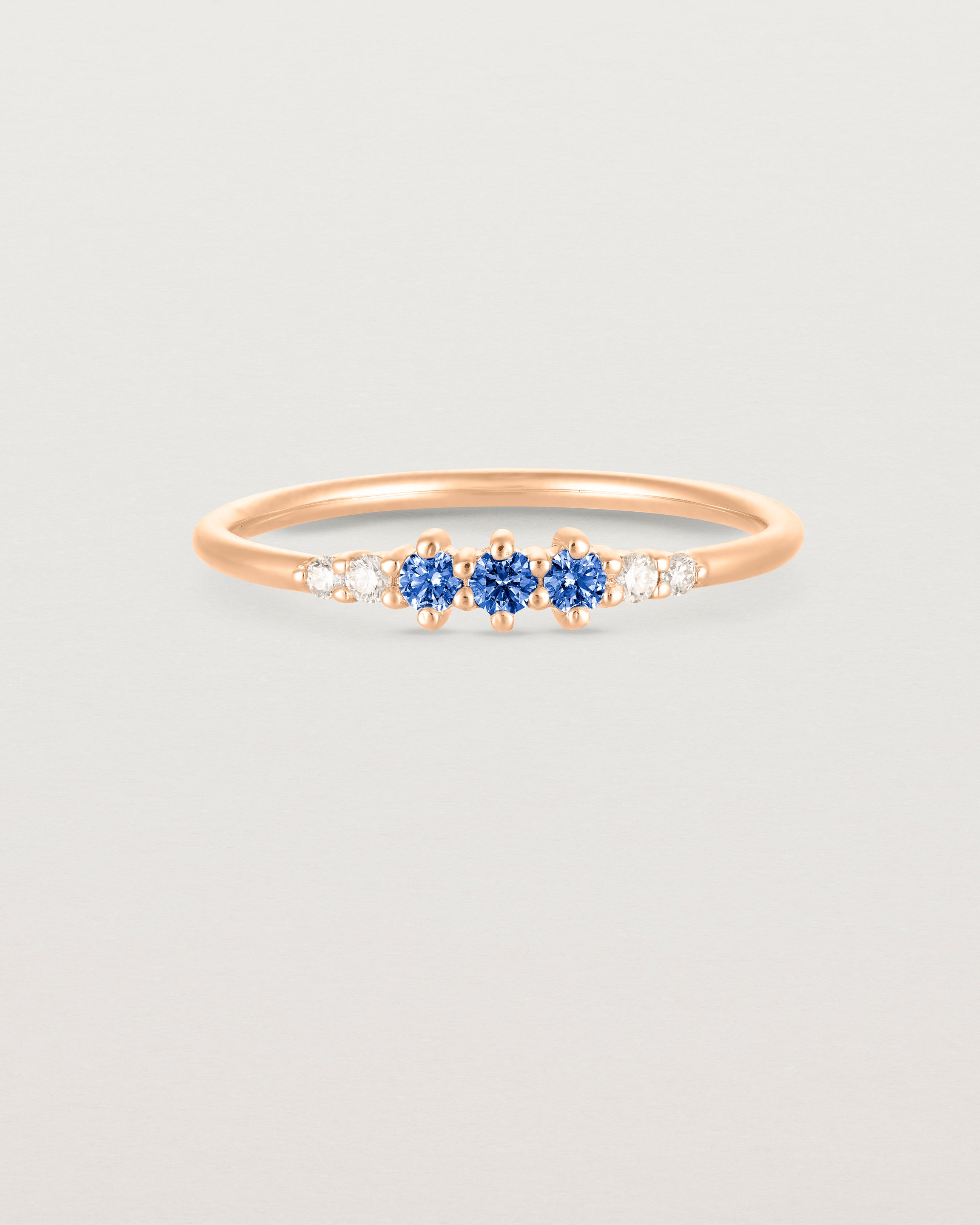 Front facing deep etched image of a rose gold ring with blue sapphire birthstones and diamonds.