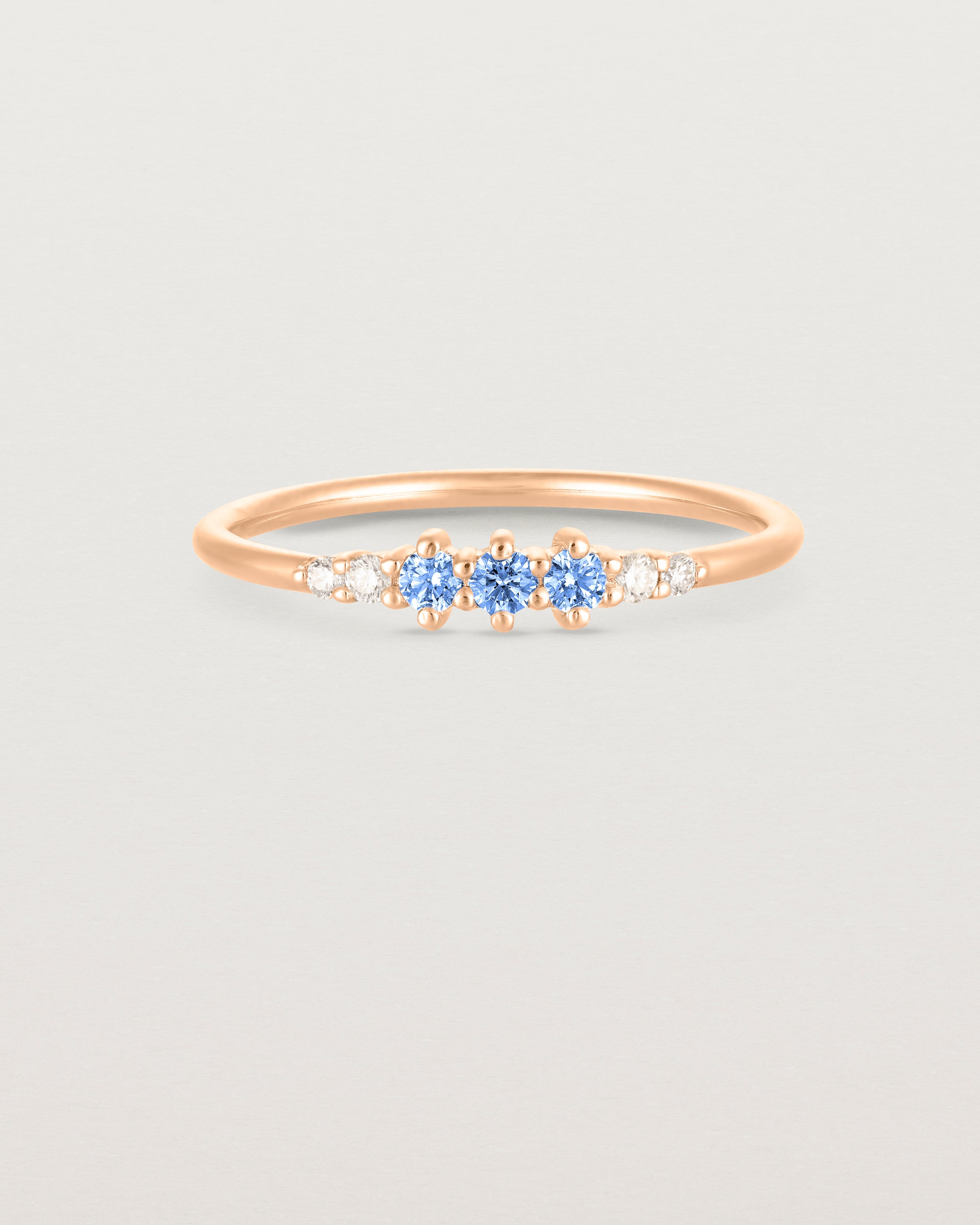 Front facing deep etched image of a rose gold ring with blue topaz birthstones and diamonds.