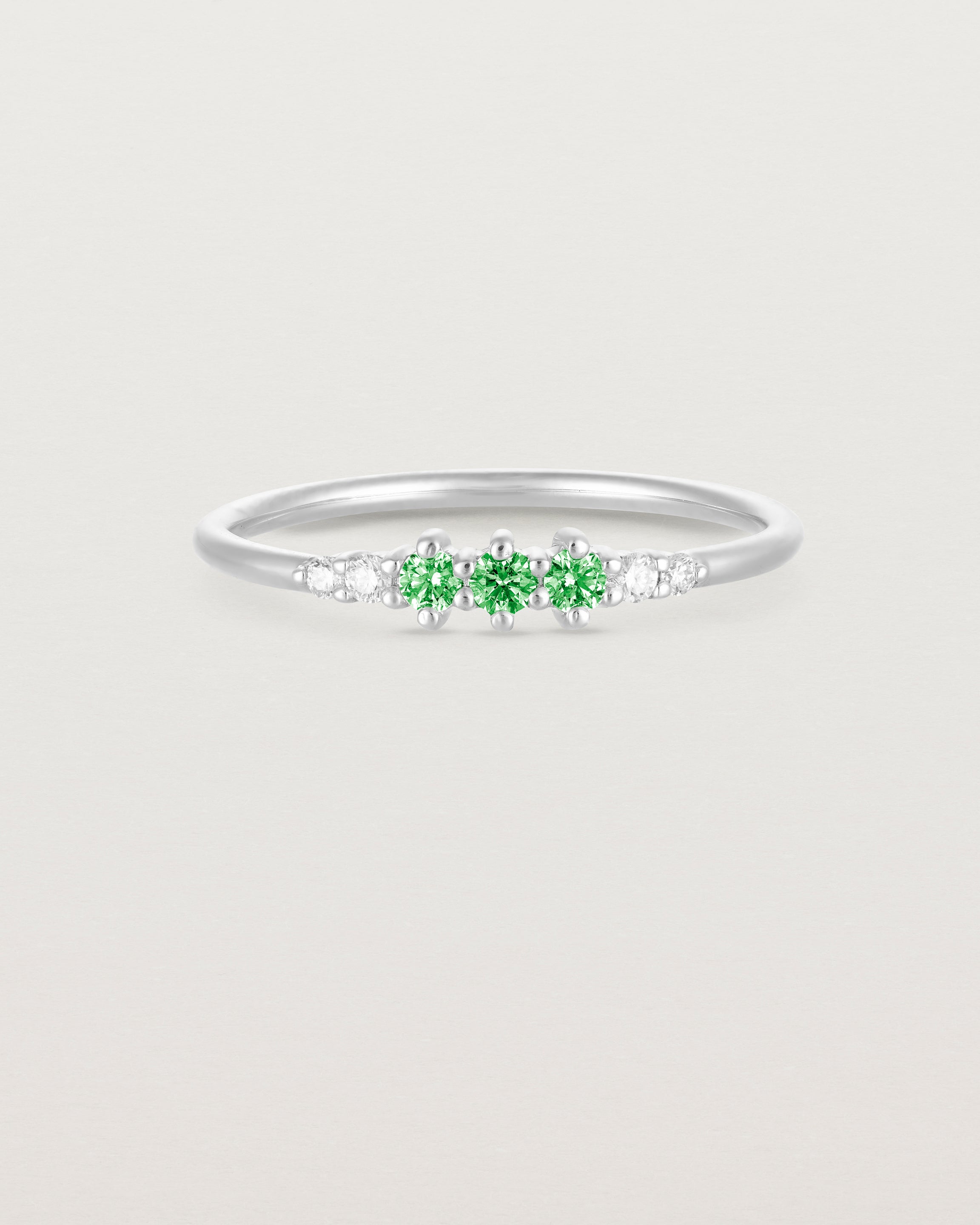 Front facing deep etched image of a white gold ring with emerald birthstones and diamonds.