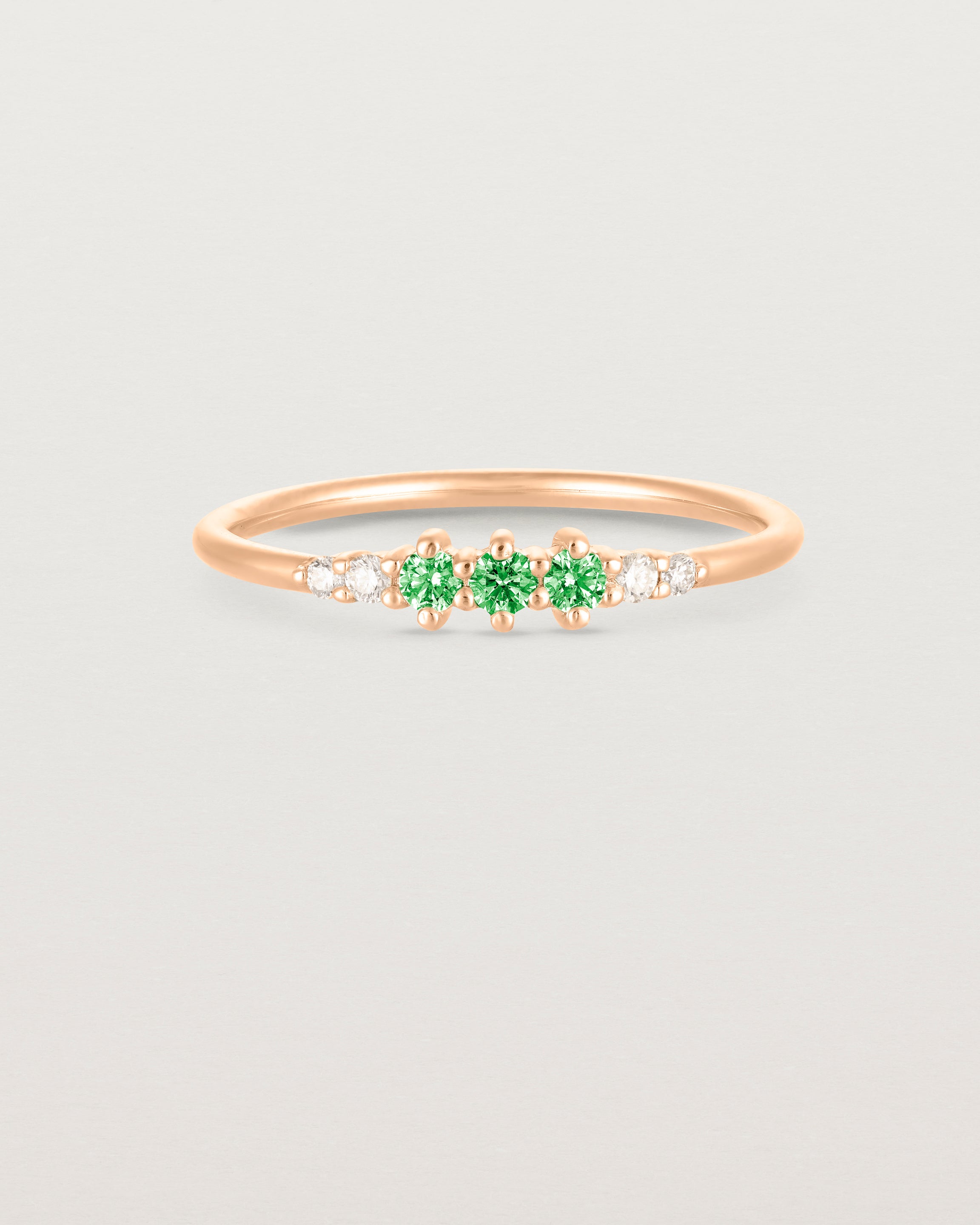 Front facing deep etched image of a rose gold ring with emerald birthstones and diamonds.