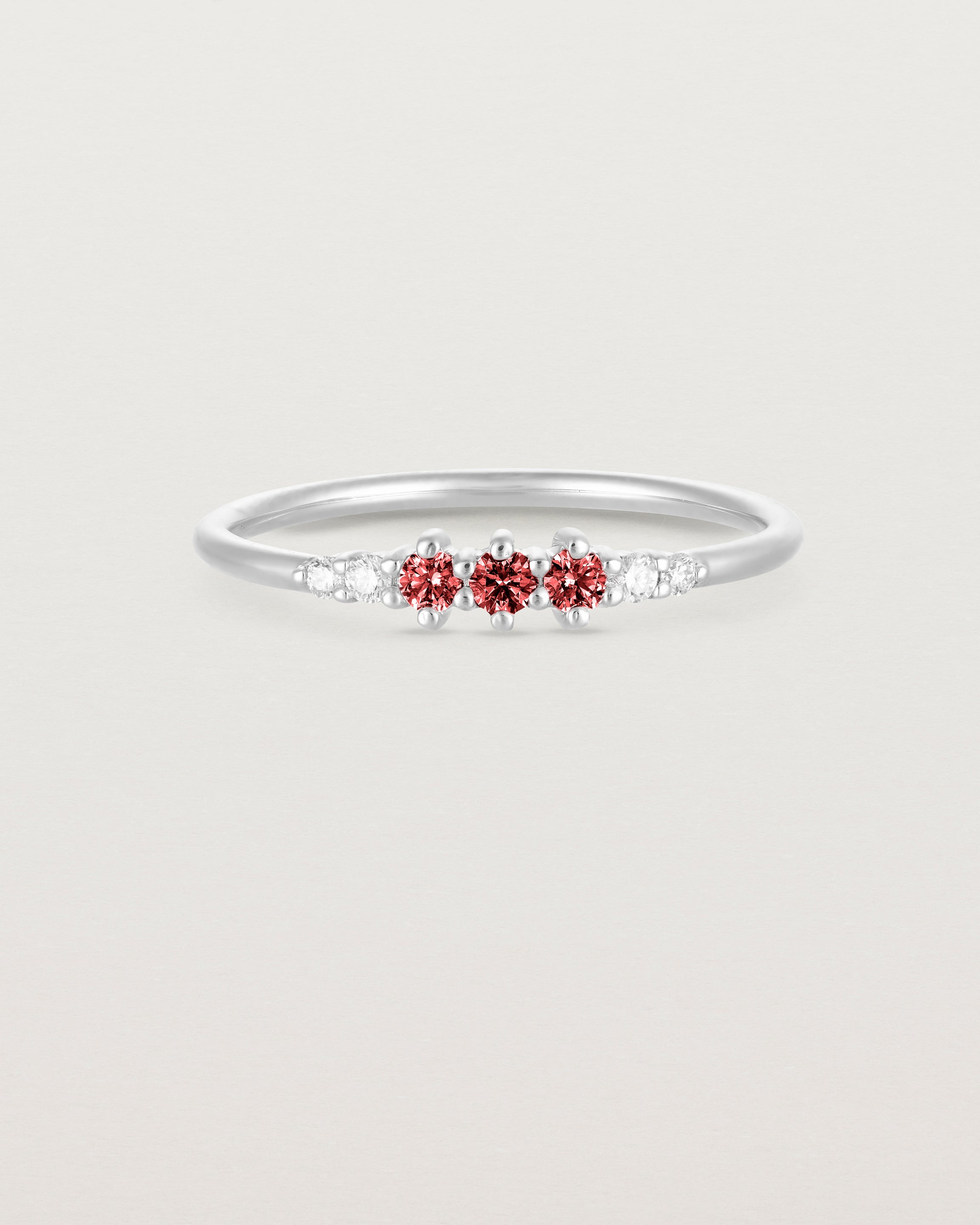 Front facing deep etched image of a white gold ring with ruby birthstones and diamonds.
