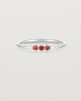 Front facing deep etched image of a white gold ring with ruby birthstones and diamonds.