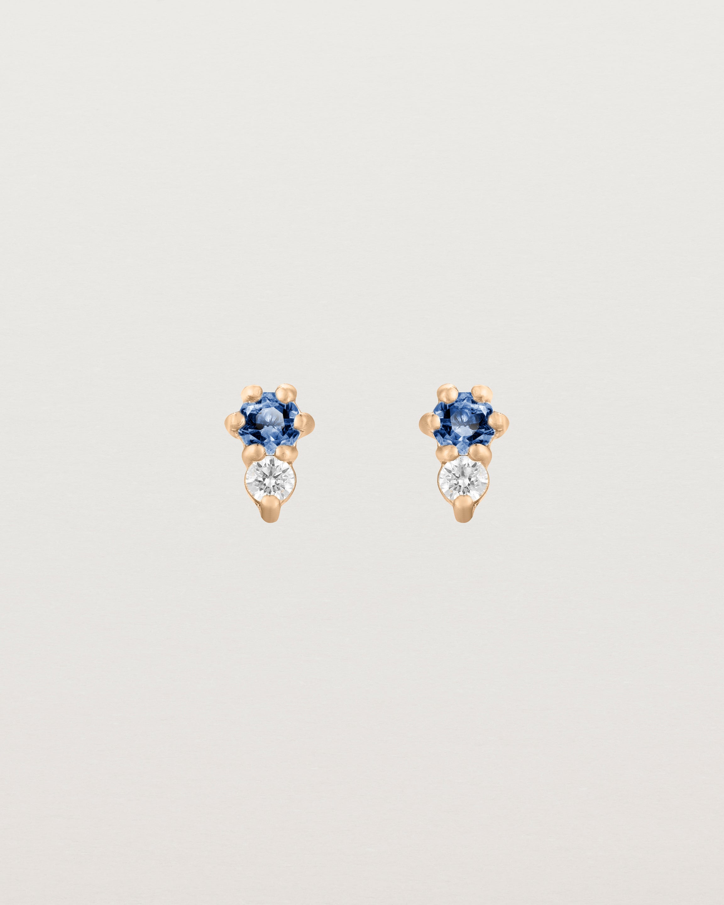 Front facing deep etched image of a pair of rose gold earrings with blue sapphire birthstones and diamonds.