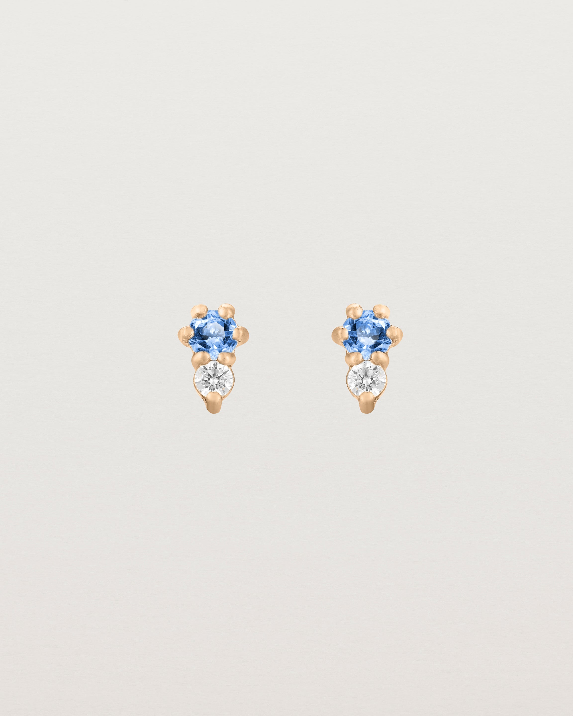 Front facing deep etched image of a pair of rose gold earrings with blue topaz birthstones and diamonds.