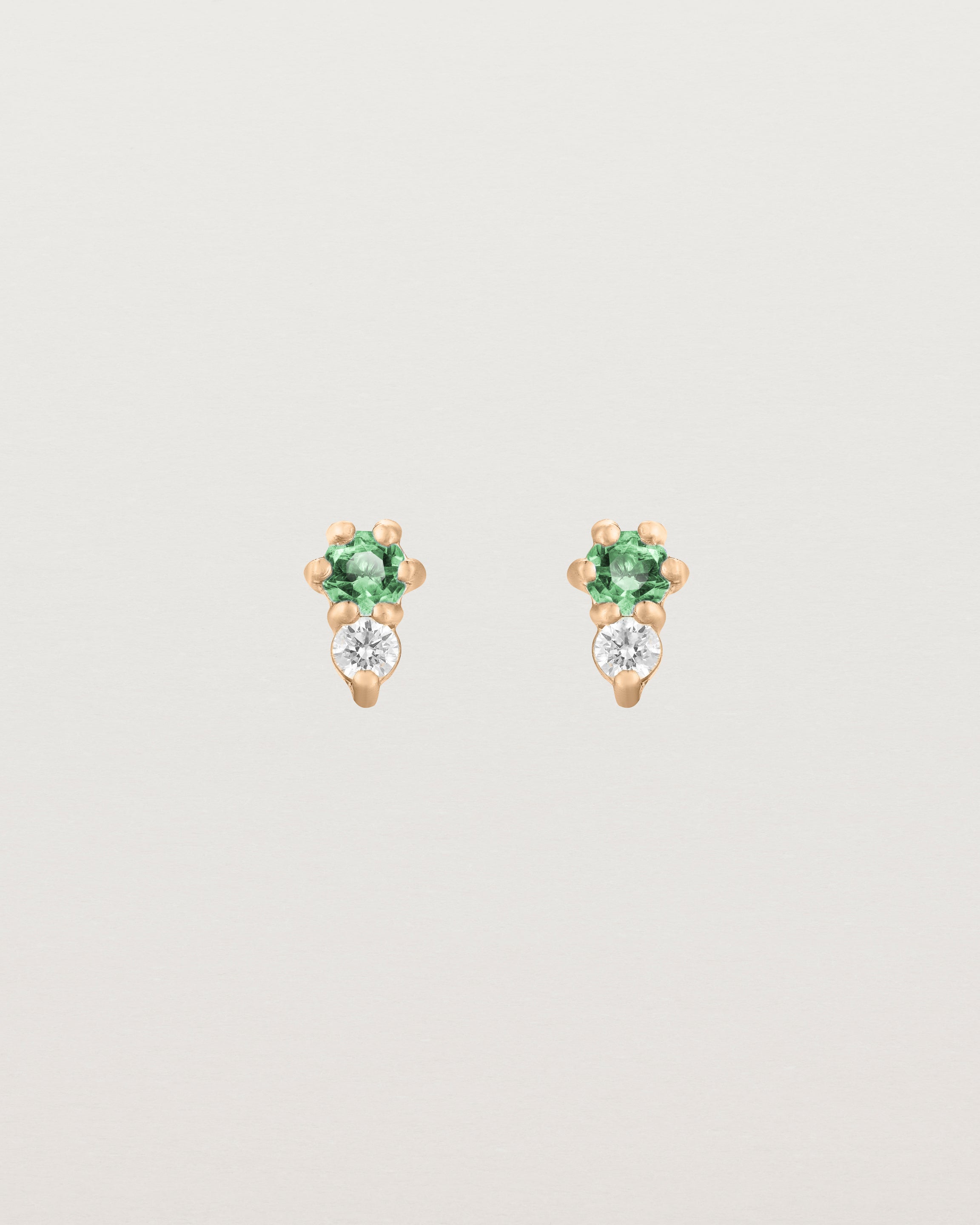 Front facing deep etched image of a pair of rose gold earrings with emerald birthstones and diamonds.