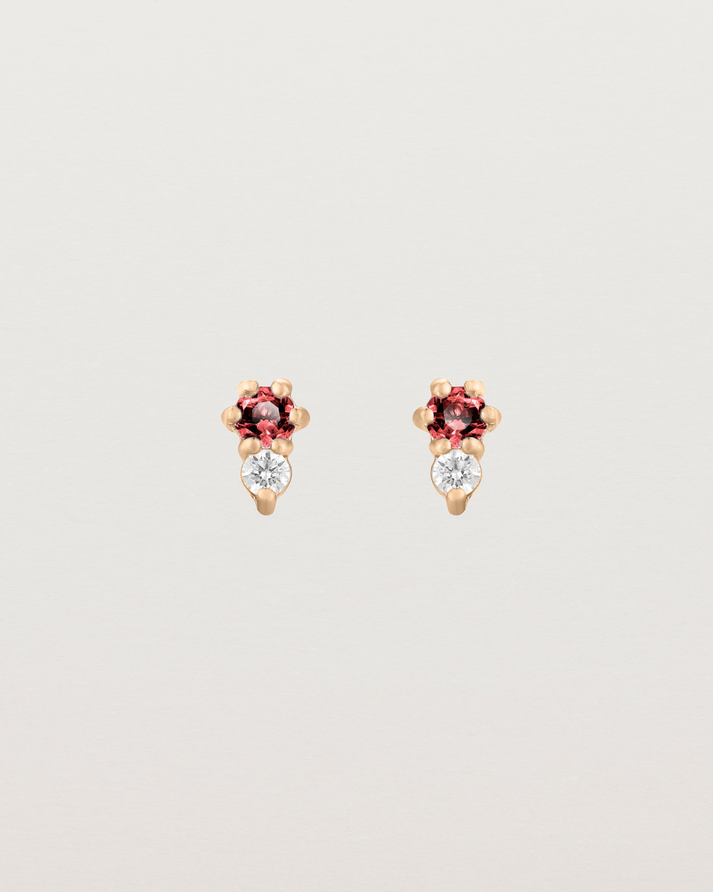 Front facing deep etched image of a pair of rose gold earrings with ruby birthstones and diamonds.