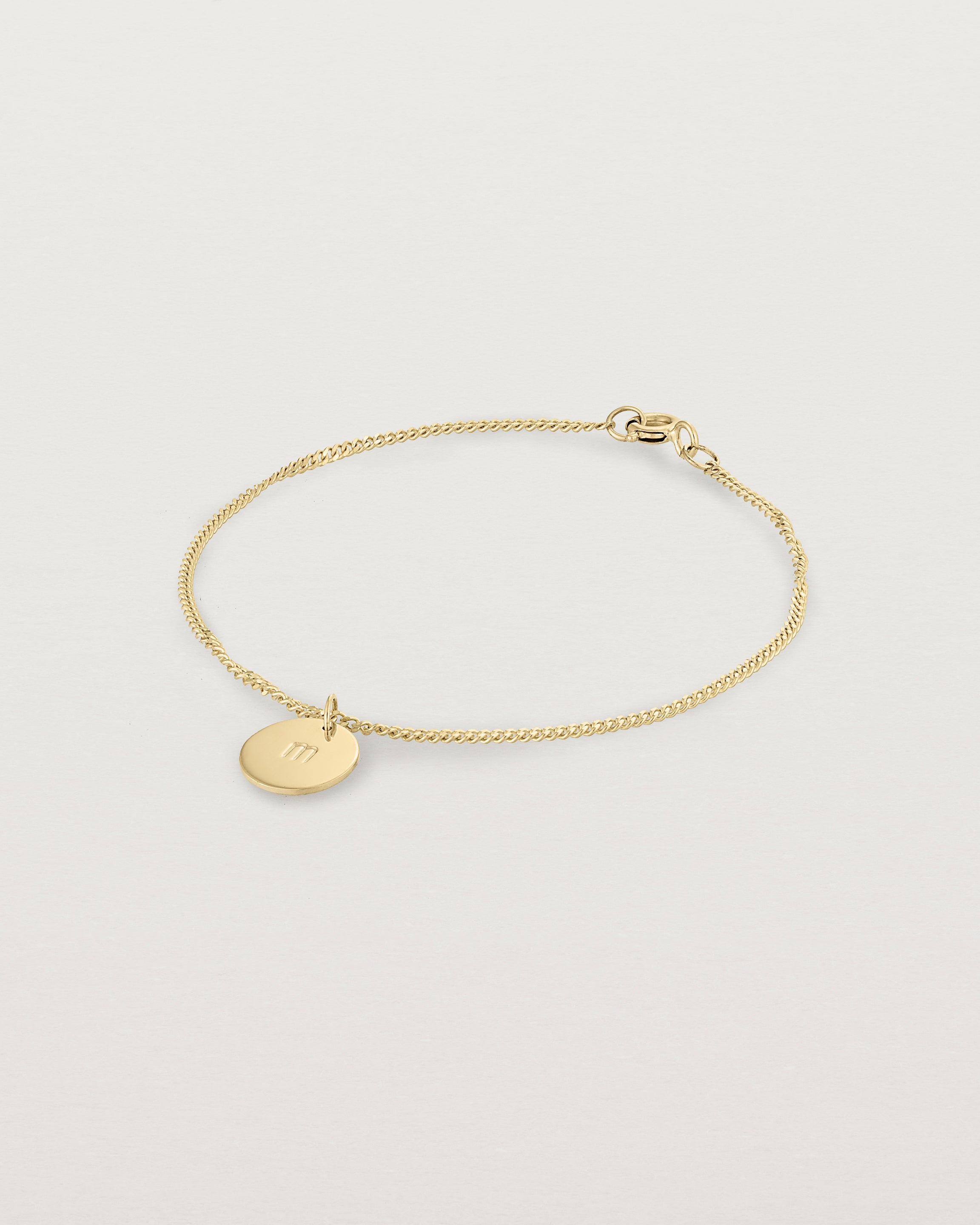 A yellow gold chain bracelet featuring a disc with an engraved letter m