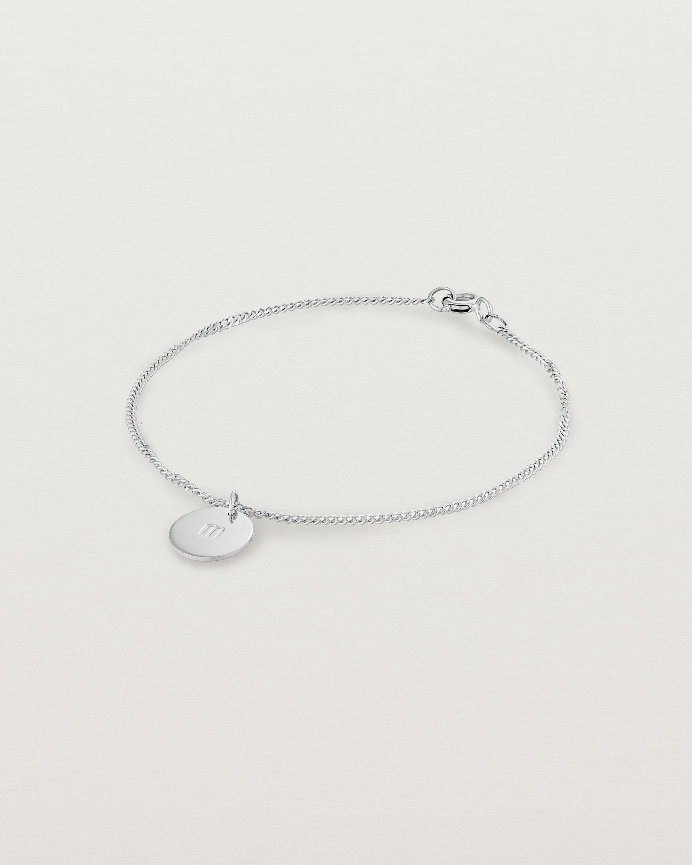 A sterling silver chain bracelet featuring a disc with an engraved letter m