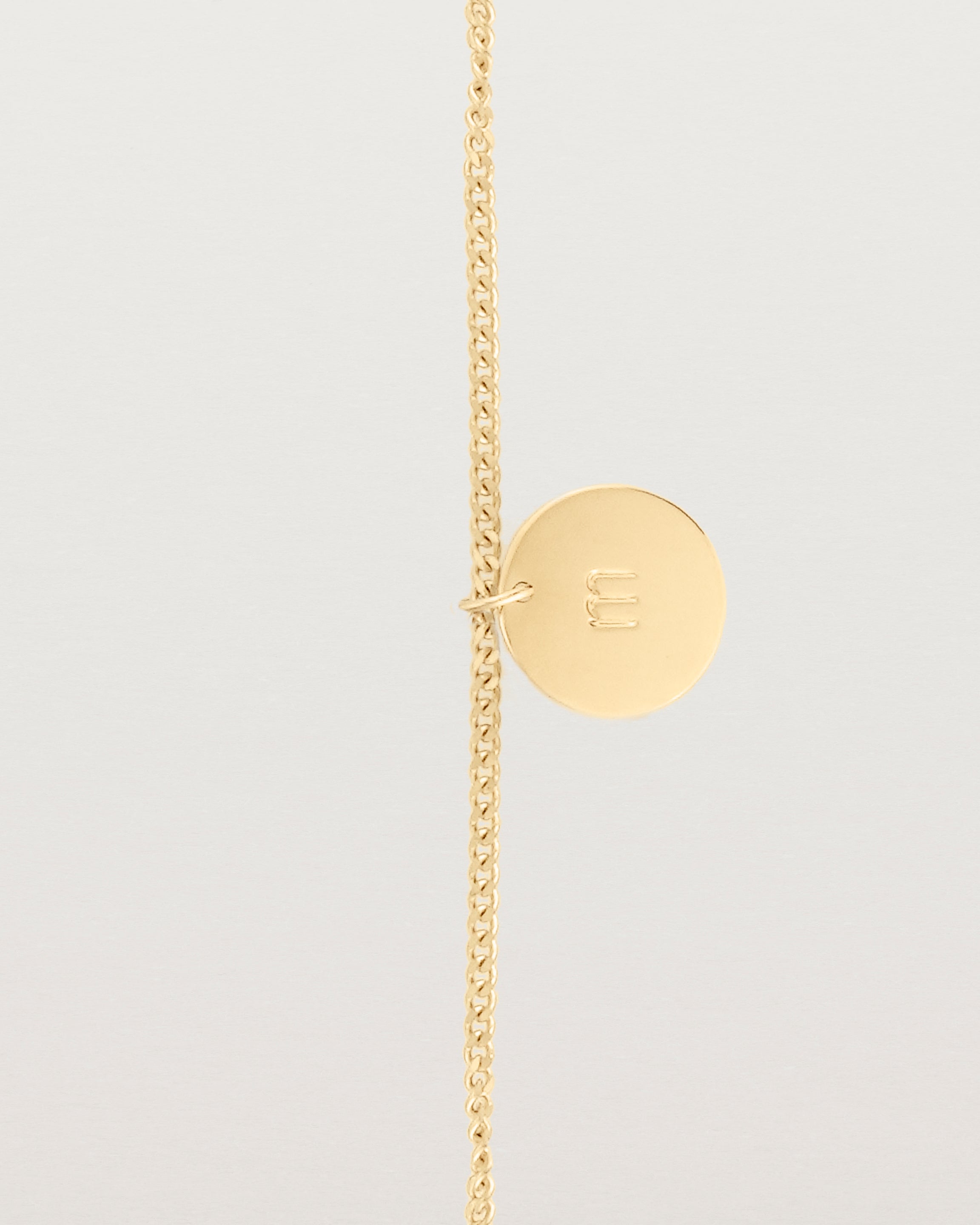 A yellow gold chain bracelet featuring a disc with an engraved letter m