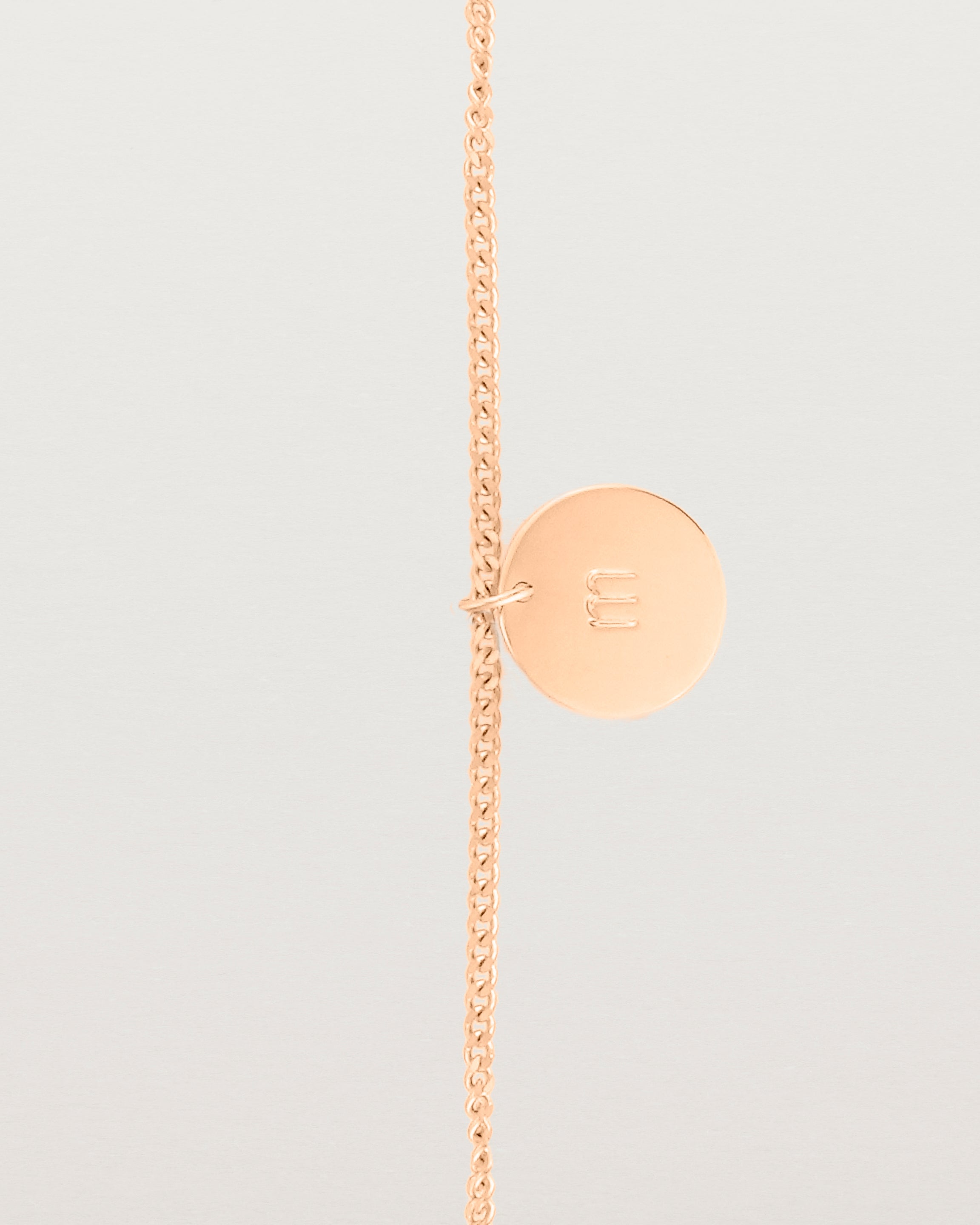 A rose gold chain bracelet featuring a disc with an engraved letter m