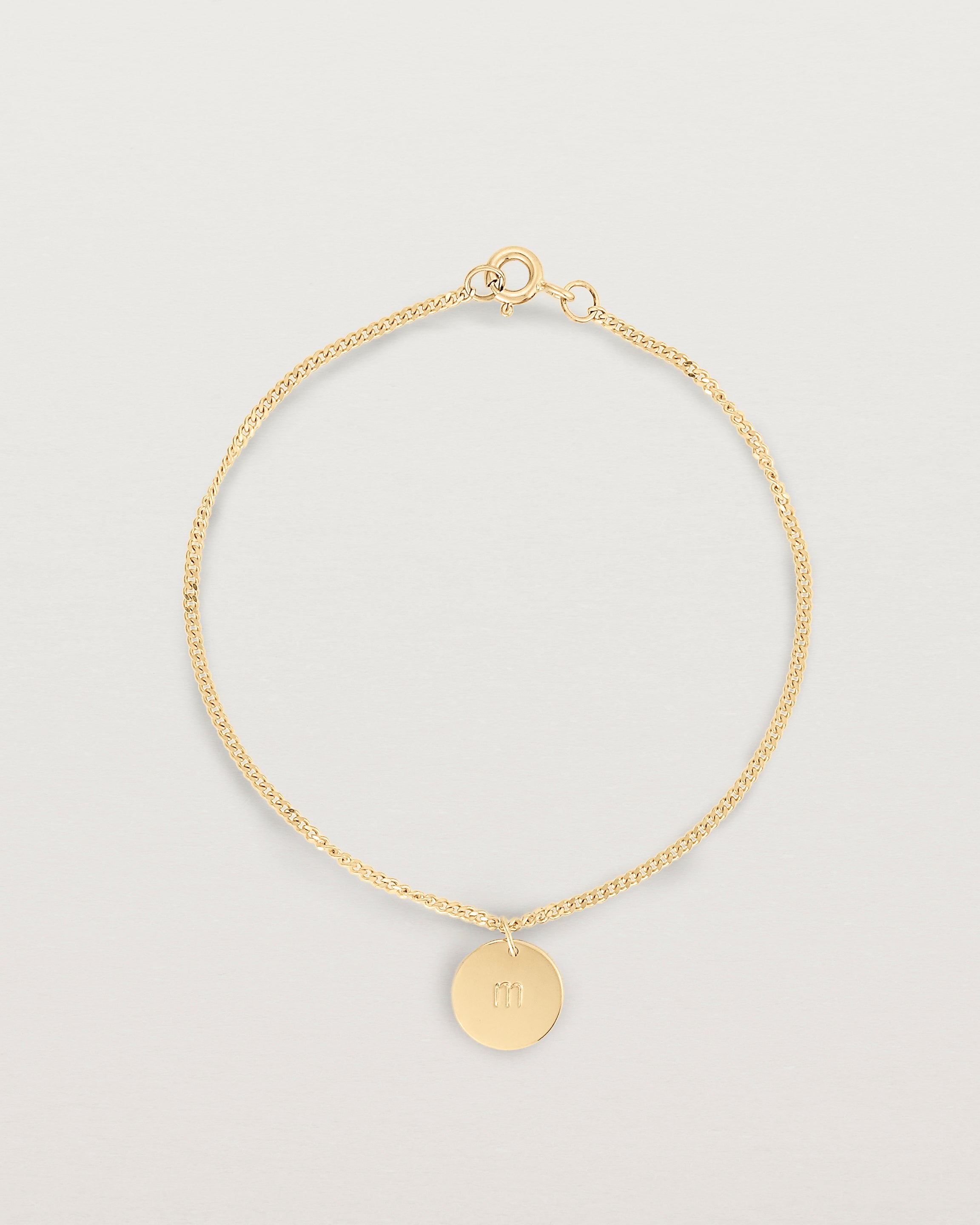 A yellow gold chain bracelet featuring a disc with an engraved letter m