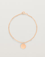 A rose gold chain bracelet featuring a disc with an engraved letter m