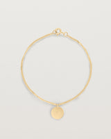 A yellow gold chain bracelet featuring a disc with an engraved letter m