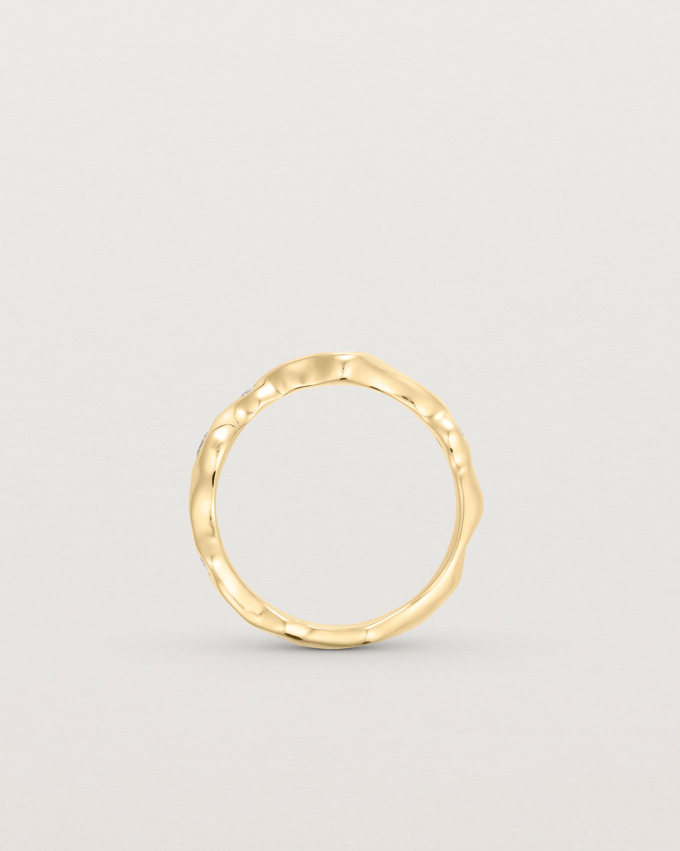 Standing deep etched image of a yellow gold ring with seven scattered white diamonds.