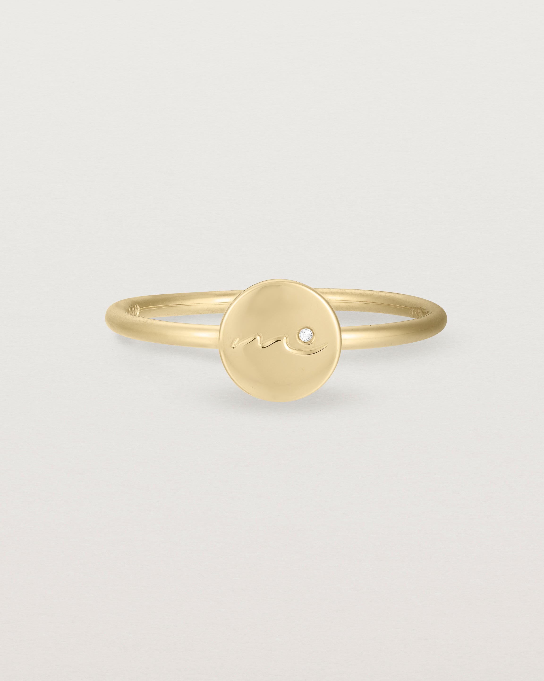 Front view of a yellow gold ring featuring a disc with the letter m engraved and a small diamond set