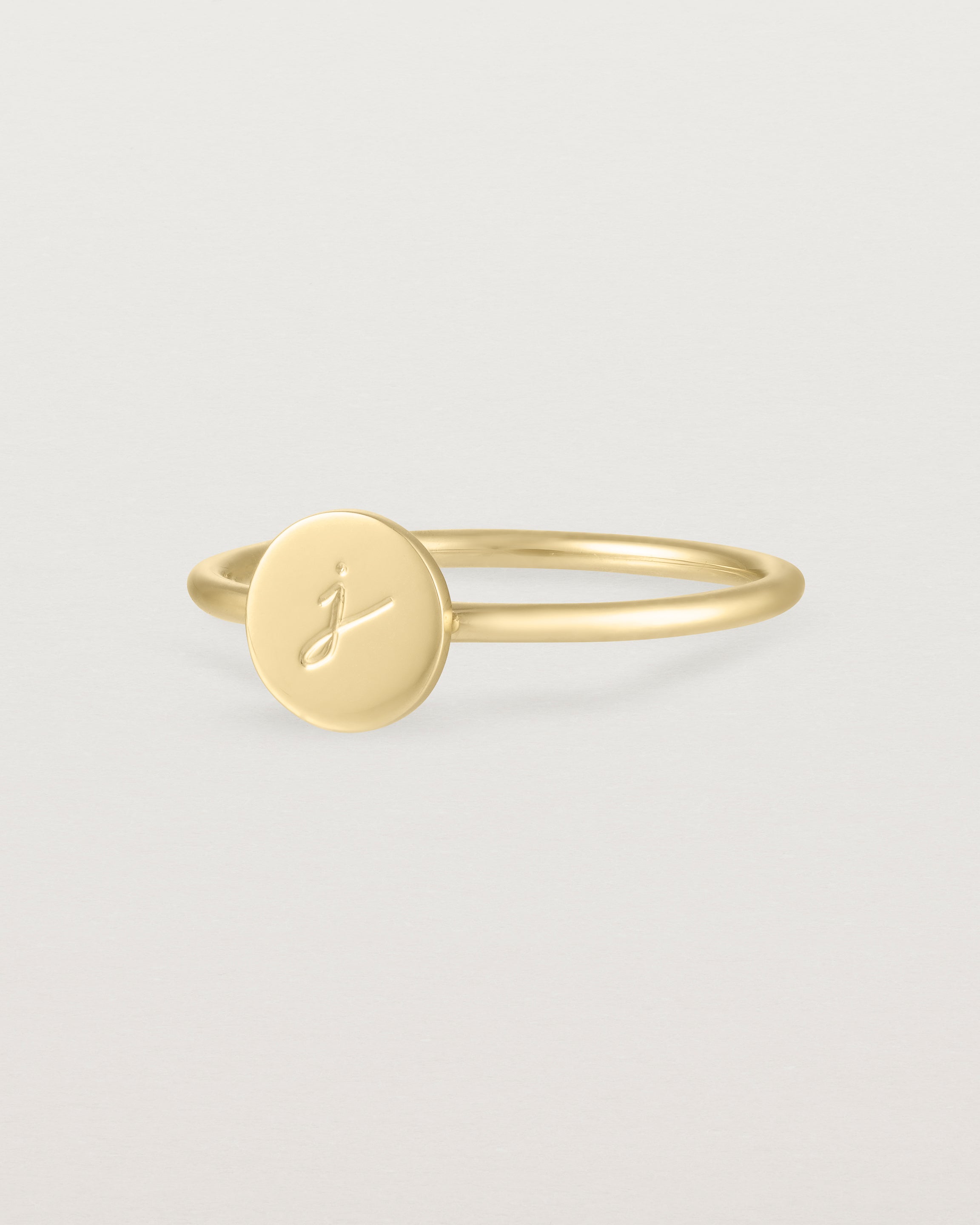 Angled view of a yellow gold ring featuring a disc with the letter j engraved
