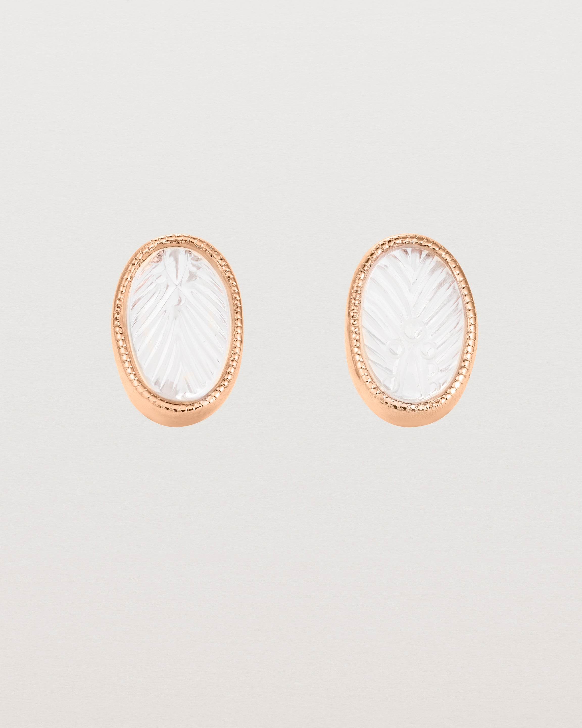 A pair of large oval rose gold studs featuring carved quartz