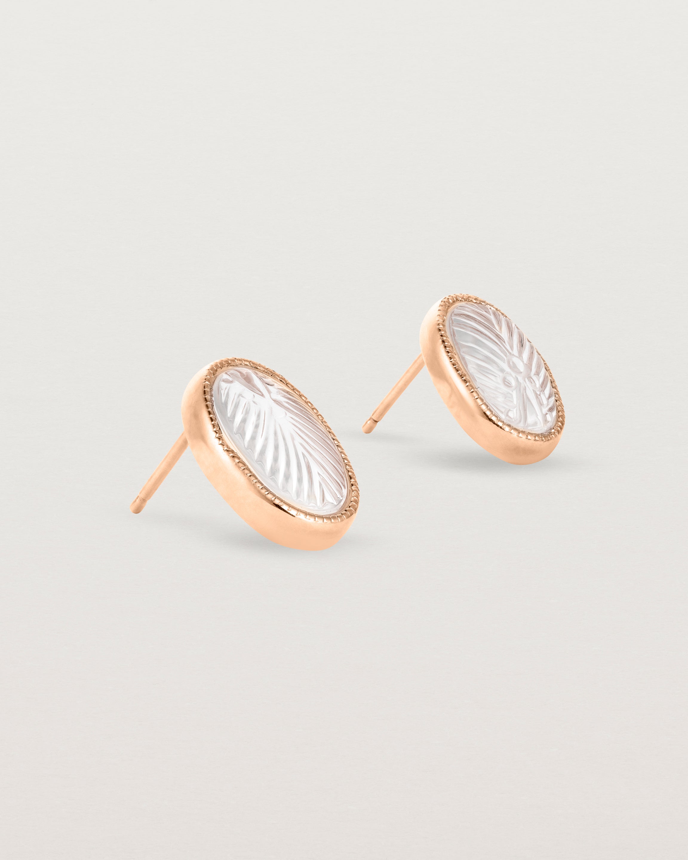 A pair of large oval rose gold studs featuring carved quartz