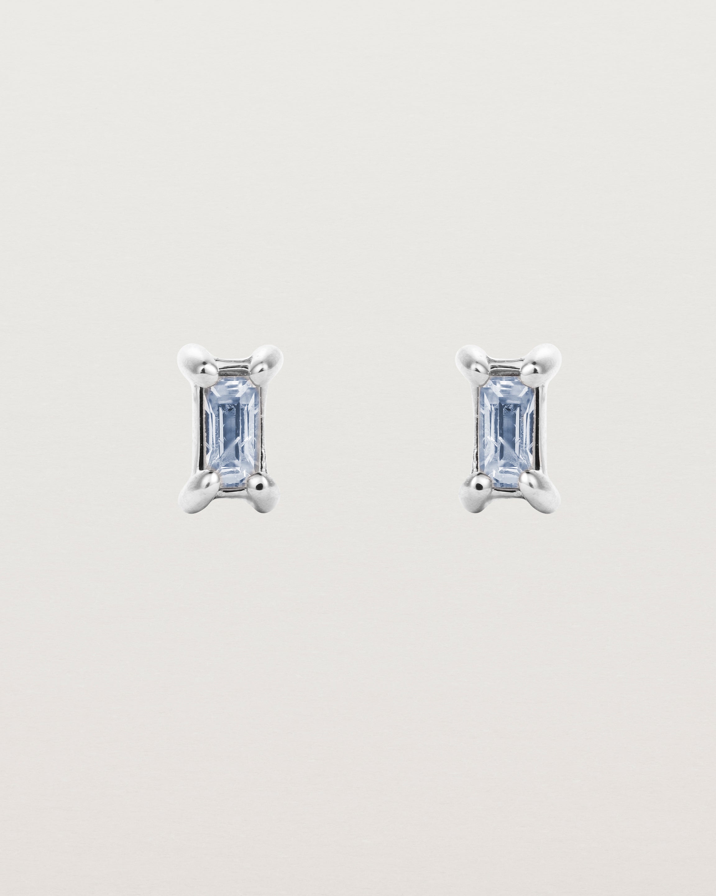 A pair of white gold studs featuring an emerald cut pale blue sapphire