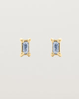 A pair of yellow gold studs featuring an emerald cut pale blue sapphire