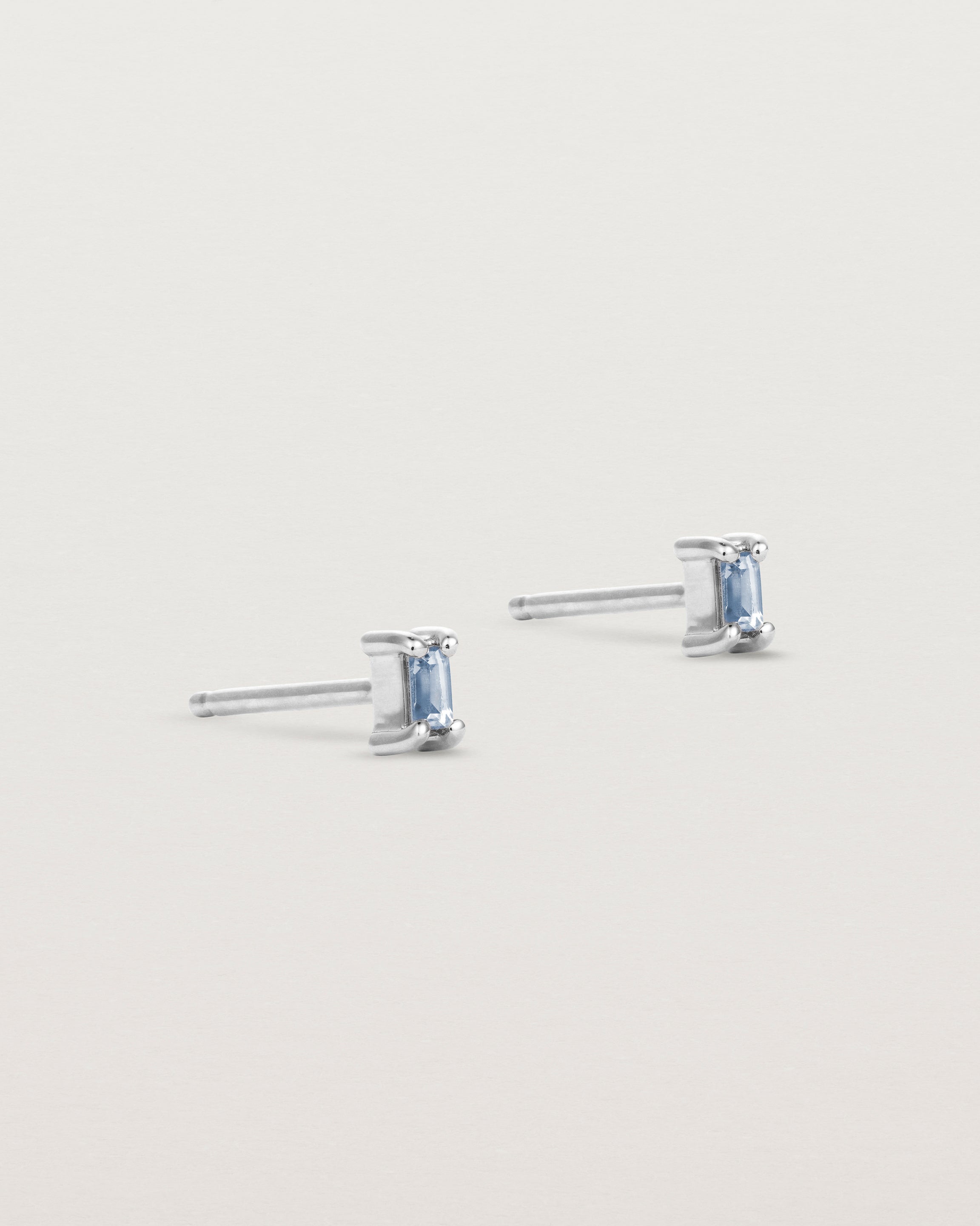 A pair of white gold studs featuring an emerald cut pale blue sapphire