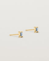 A pair of yellow gold studs featuring an emerald cut pale blue sapphire