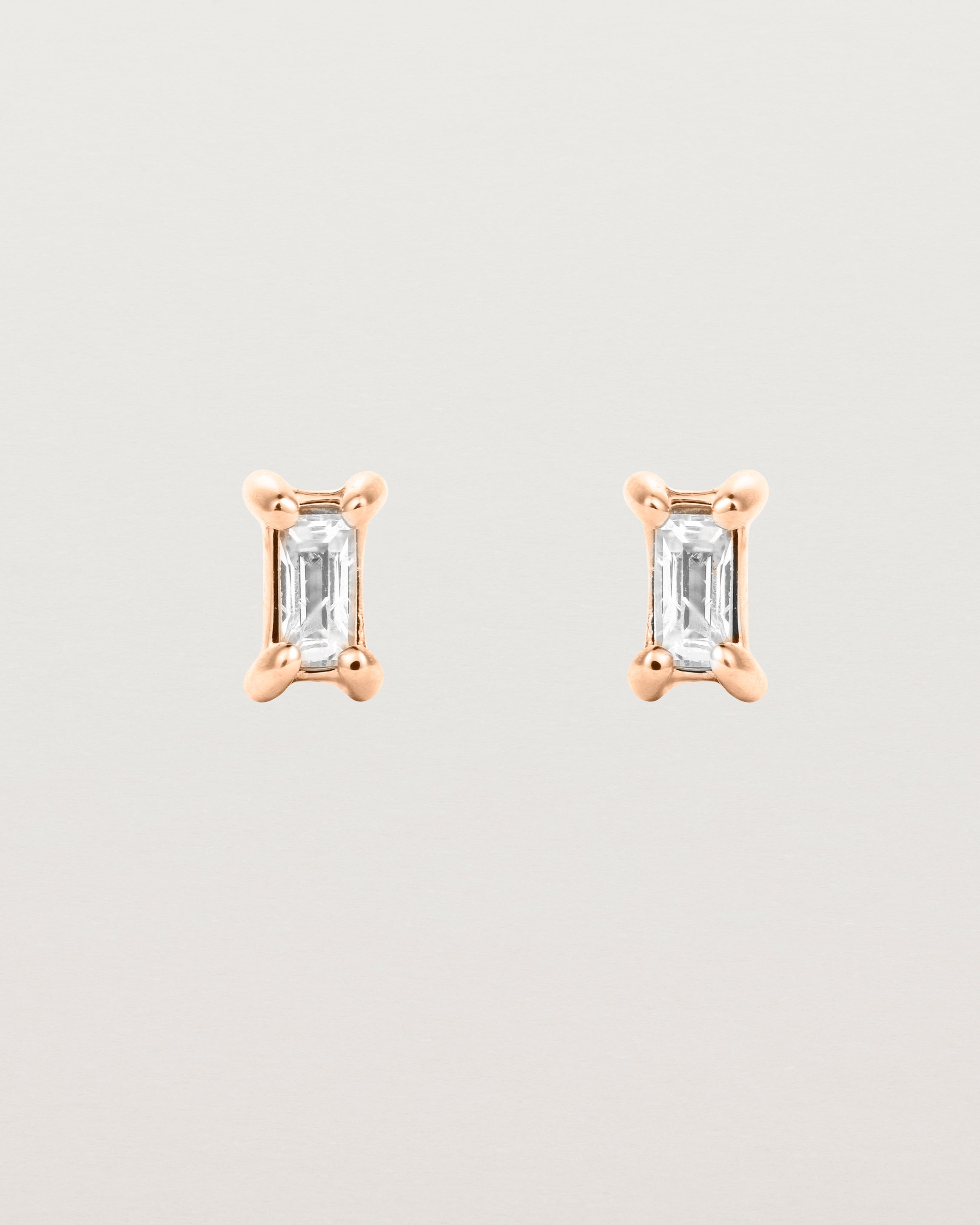 A pair of rose gold studs featuring an emerald cut white diamond