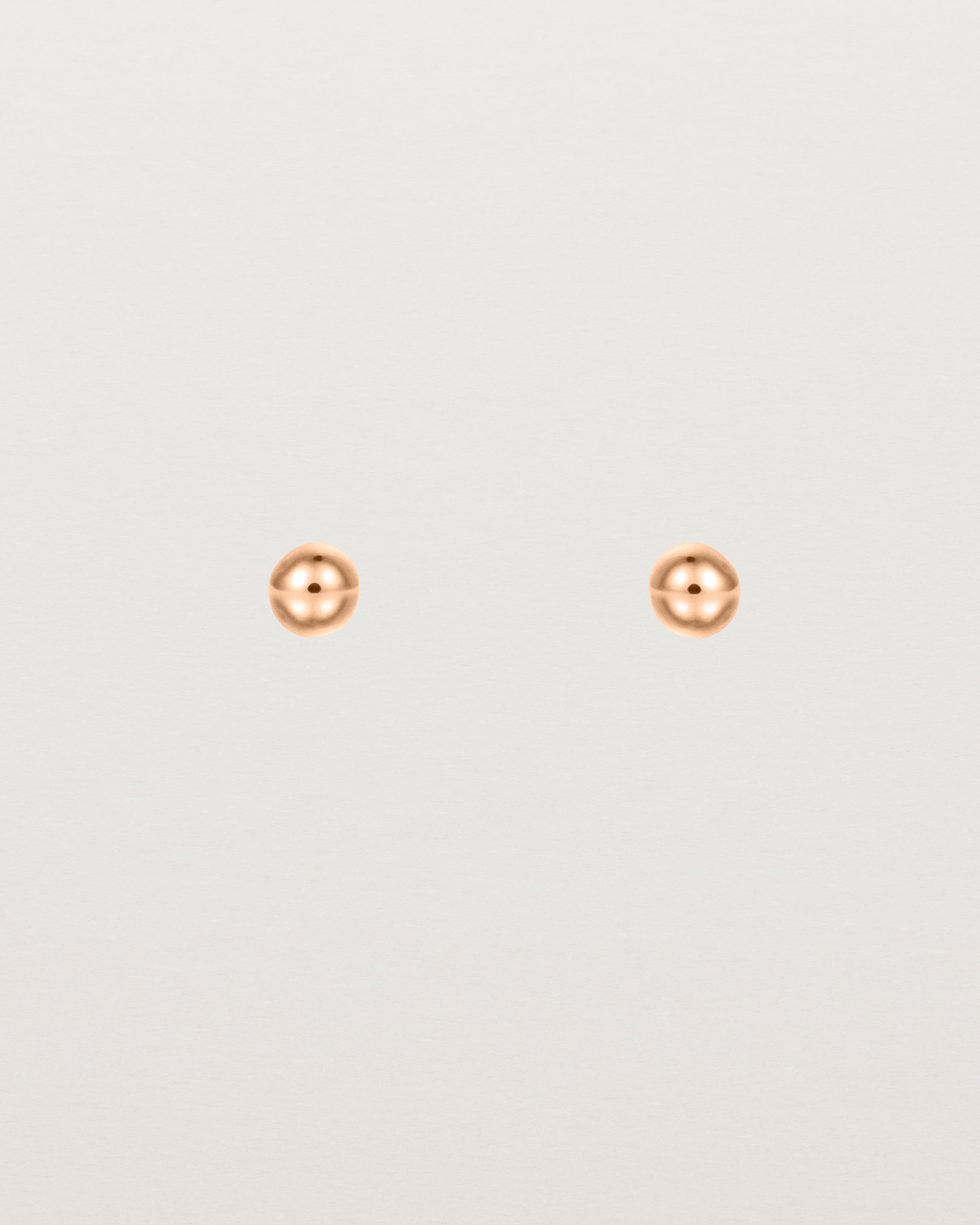 A pair of tiny rose gold studs featuring a round ball