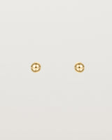 A pair of tiny yellow gold studs featuring a round ball