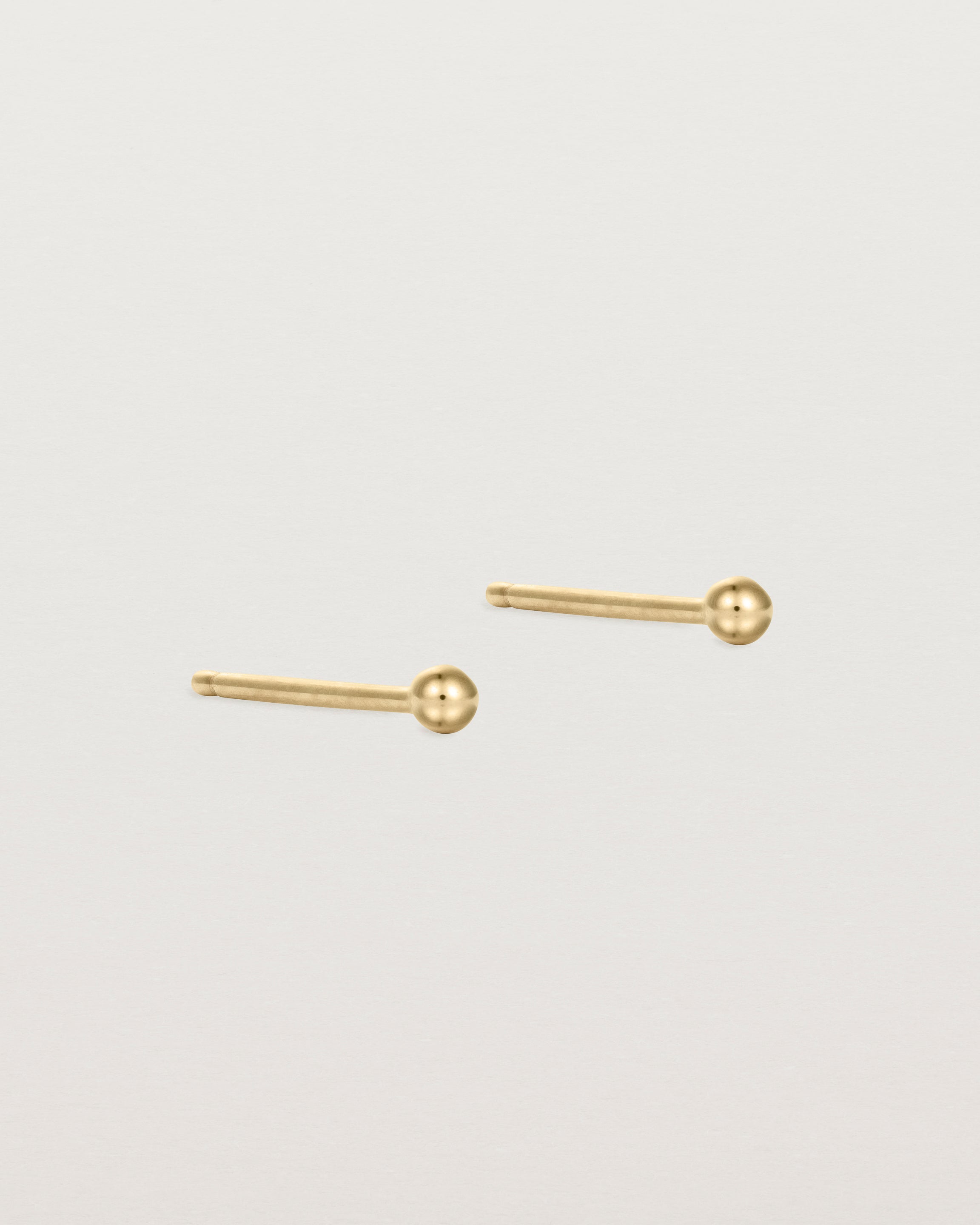 A pair of tiny yellow gold studs featuring a round ball