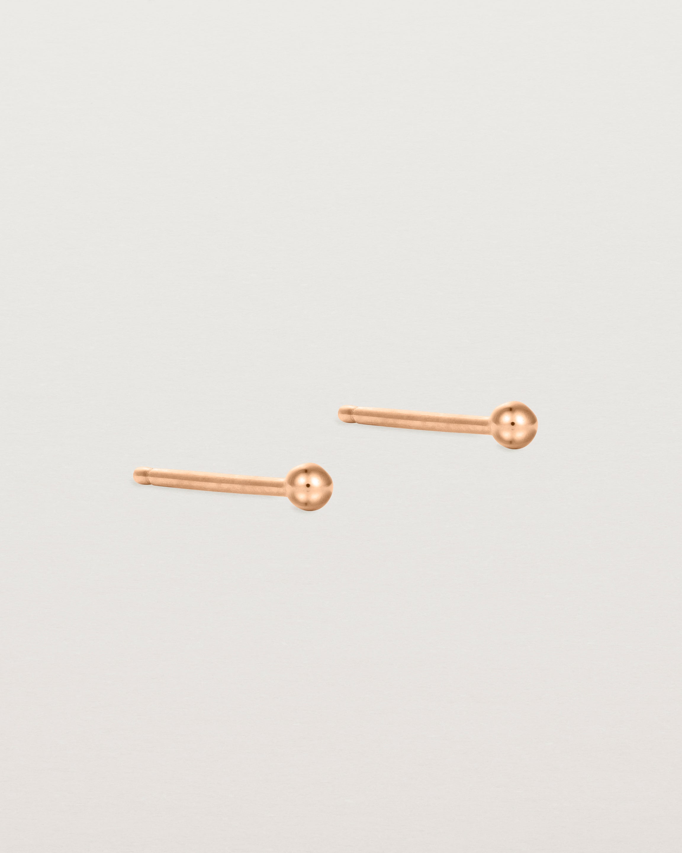 A pair of tiny rose gold studs featuring a round ball