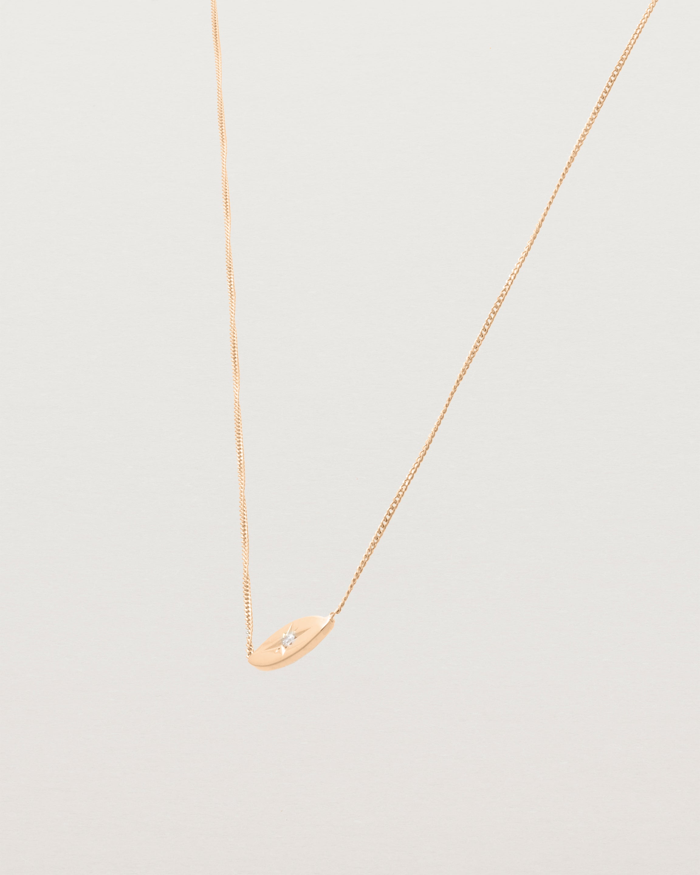 A rose gold marquise disc hung on a necklace featuring a small star set white diamond