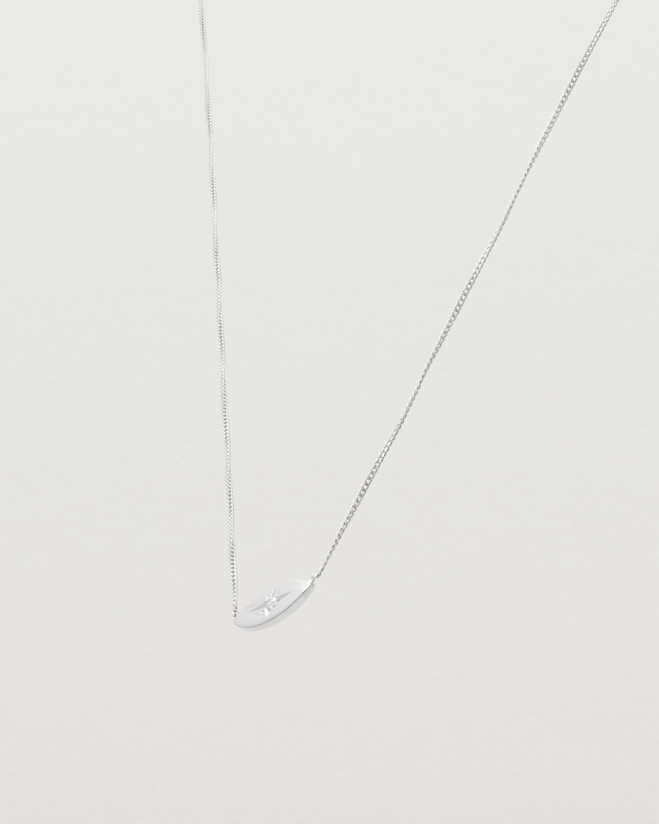 A white gold marquise disc hung on a necklace featuring a small star set white diamond