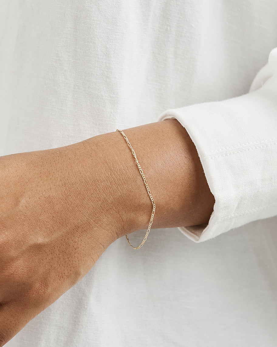 A woman wearing the Fine Figaro Chain Bracelet in yellow gold.