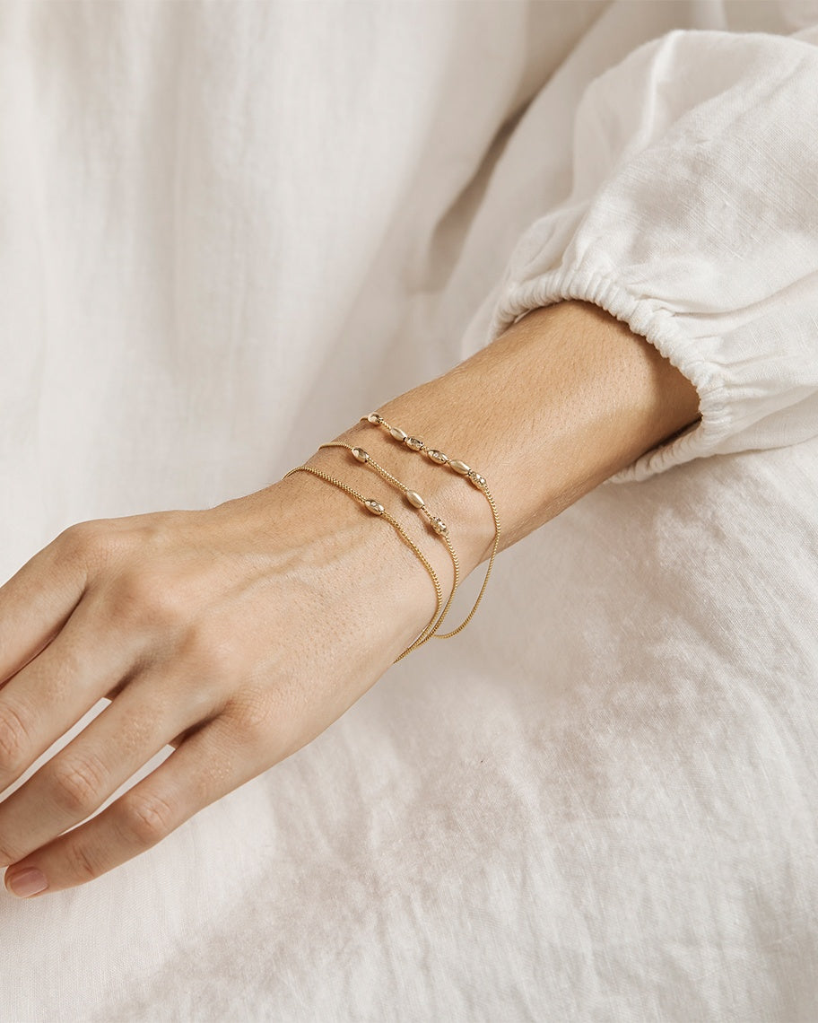 A woman wearing three Sonder Bracelets in yellow gold with different numbers of charms.